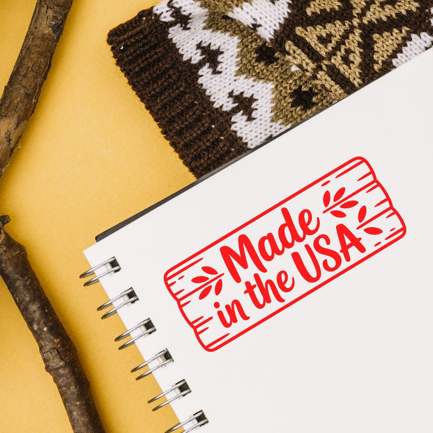 White spiral notebook featuring a red Made in the USA stamp seal, on yellow background with brown-and-white knit swatch.
