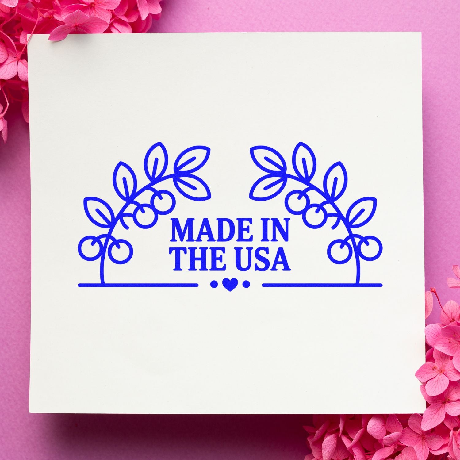 Blue Made in the USA stamp and seal with leafy wreath on white card, framed by pink flowers.