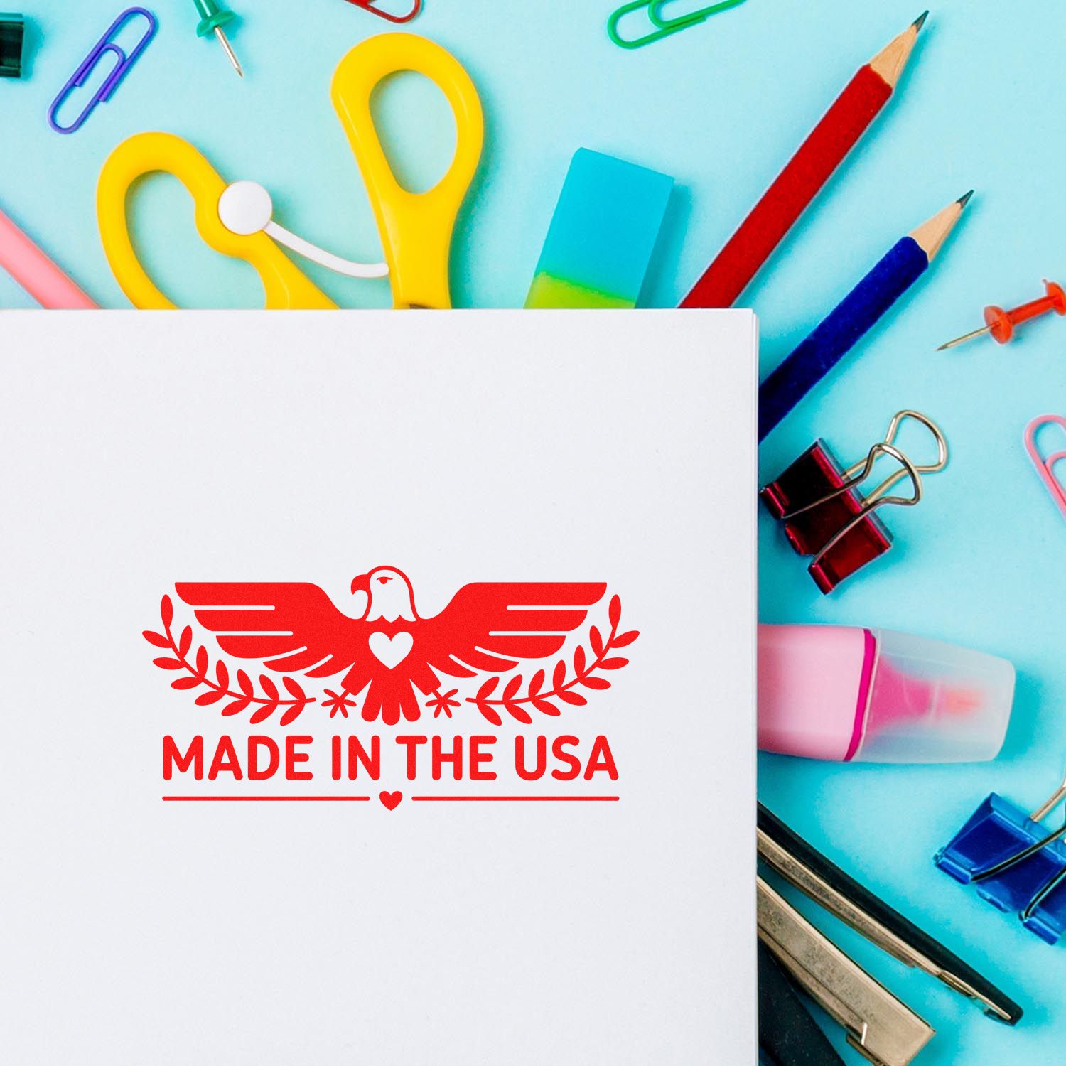 White stamp sheet with red Made in the USA seal, surrounded by colorful office supplies on a blue background.