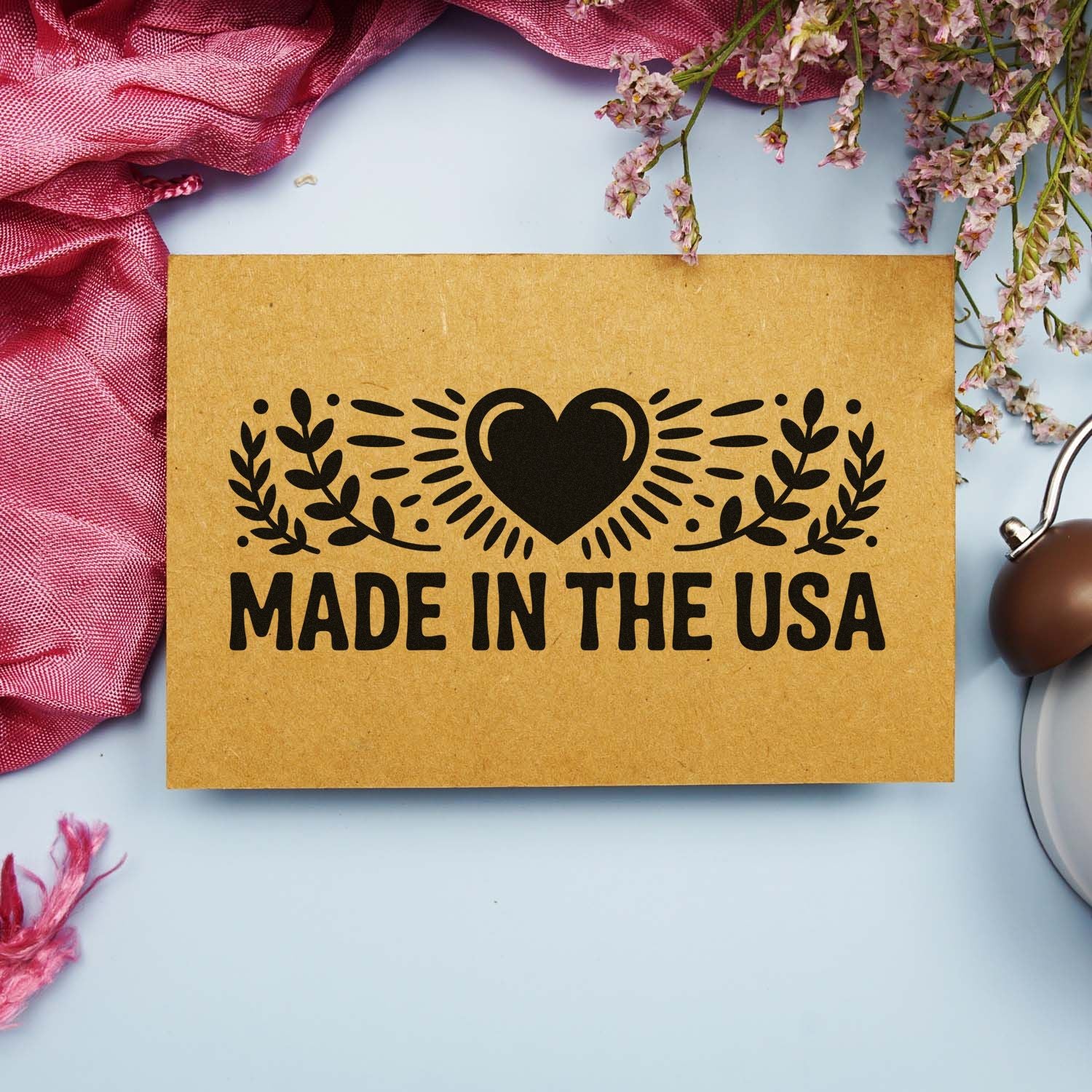 Brown kraft paper stamp seal with black heart and laurel design, Made in the USA, on pale blue with pink florals.