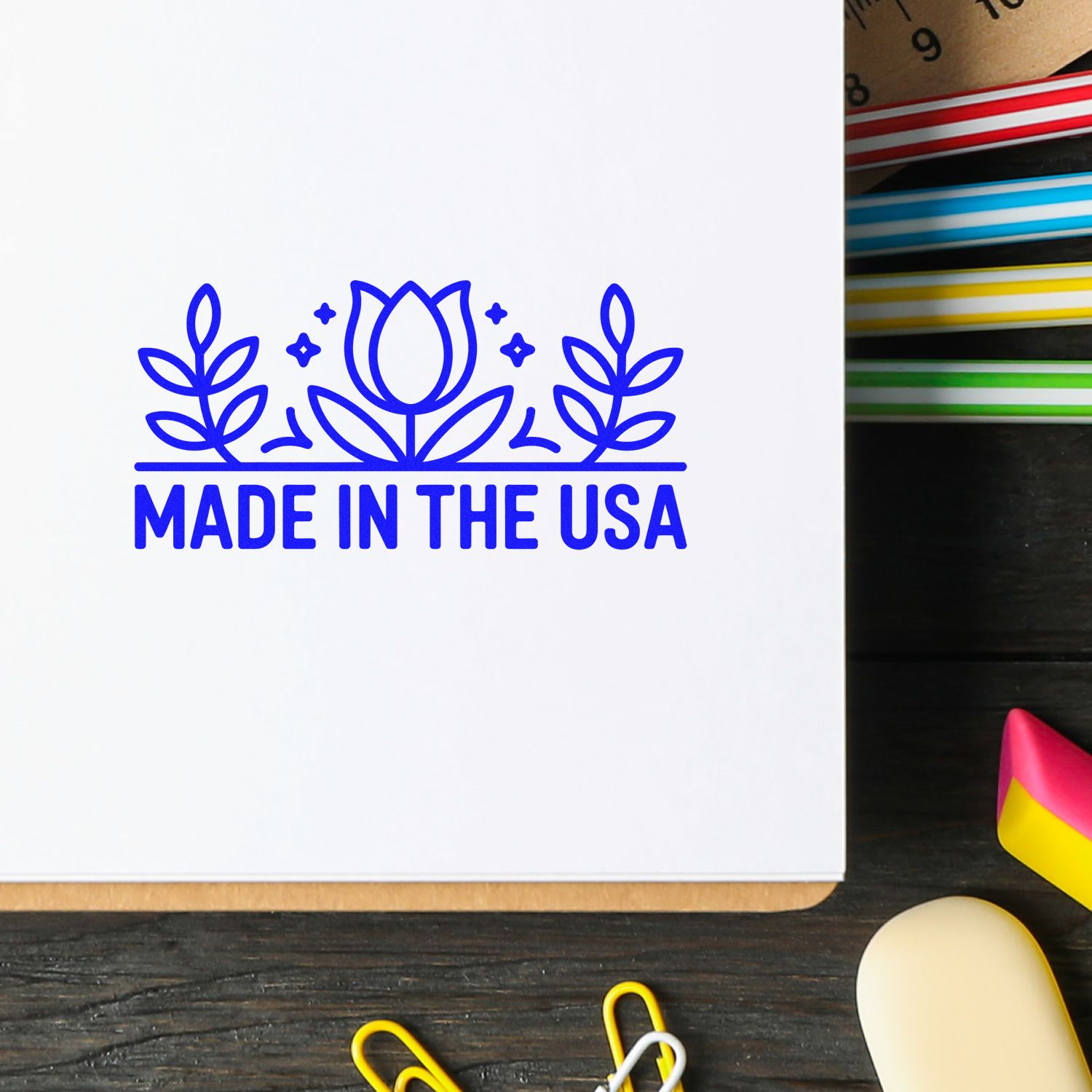 Blue Made in the USA stamp seal with floral design on white paper, beside colorful ink pads.