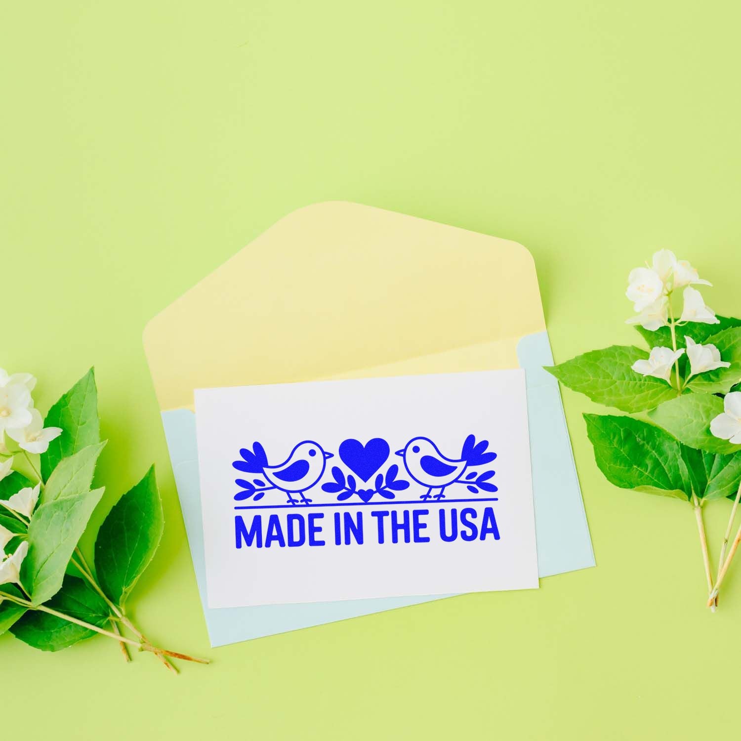 Blue Made in the USA stamp seal with birds and heart on white card, on pastel envelopes with green leaves and flowers.
