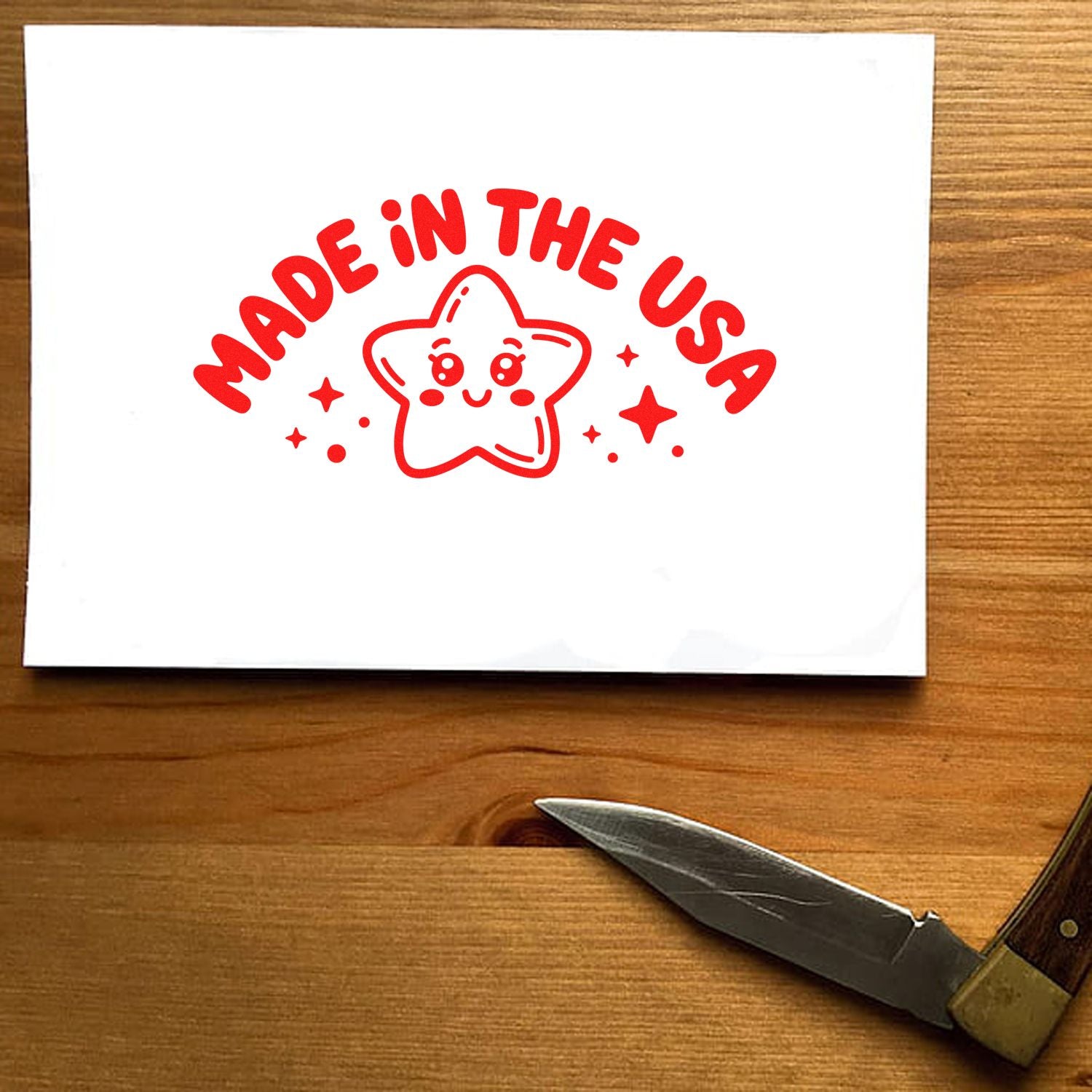 Red Made in the USA stamp and seal with smiling star and sparkles on white paper, on a wooden table.