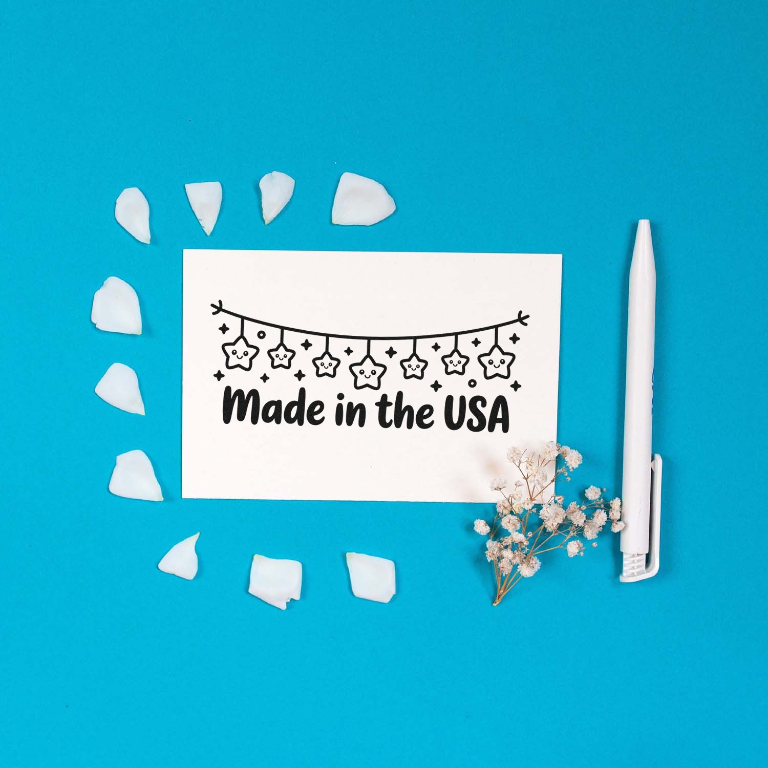 White Made in the USA stamp card on bright blue background, with white seal pieces, a white stamp pen, and dried flowers.
