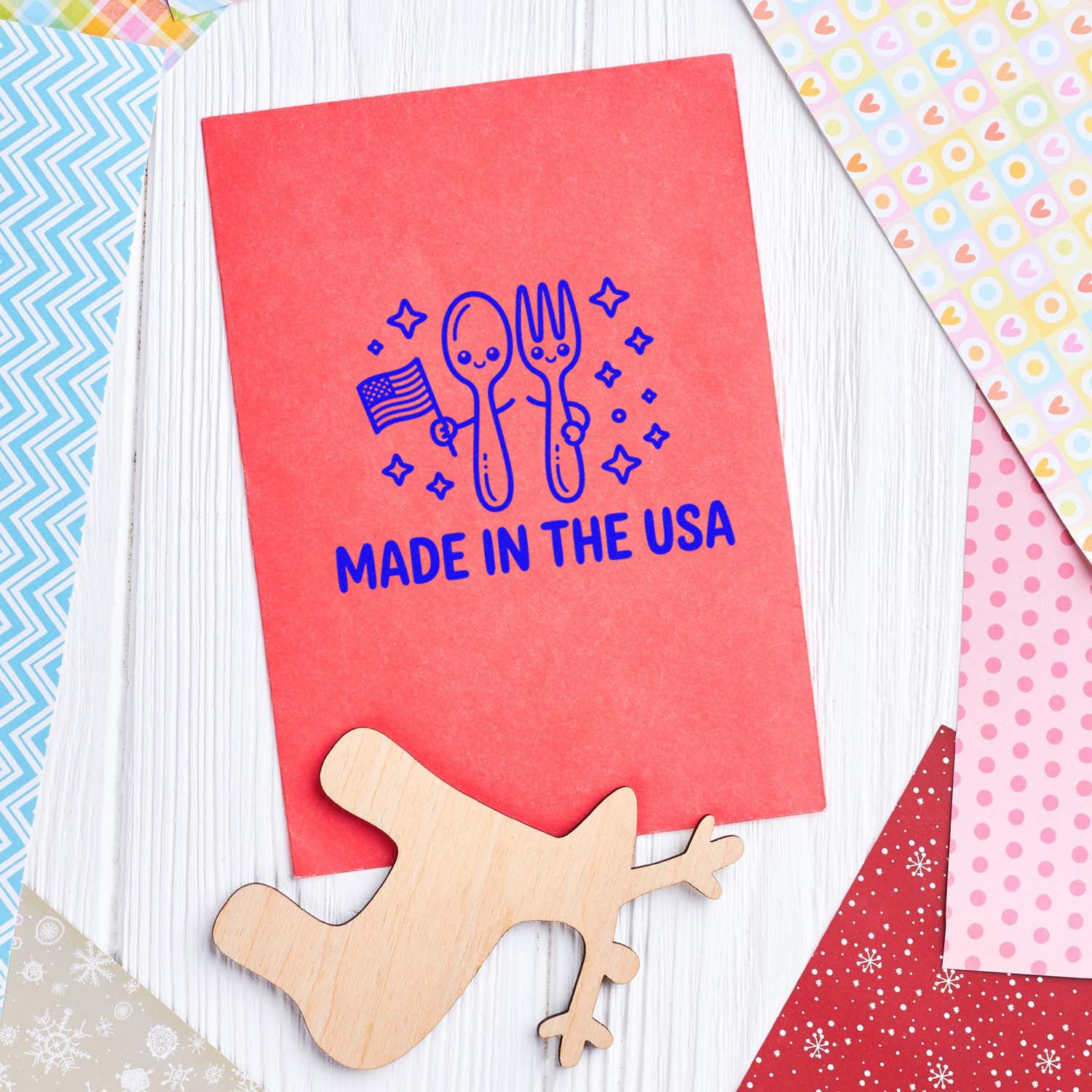Red card with blue Made in the USA stamp and seal design, spoon-and-fork icon, and wooden stamp seal on white wood.