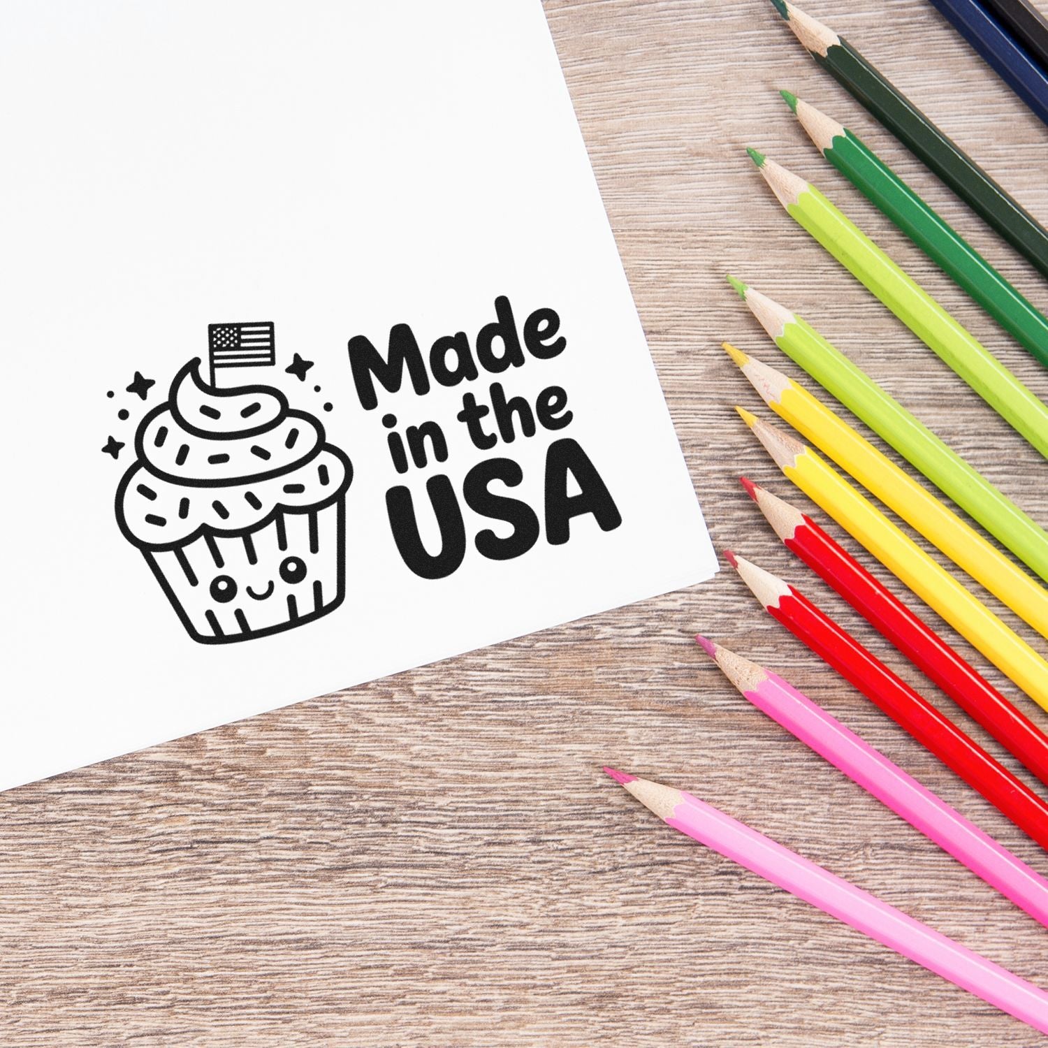Black Made in the USA cupcake stamp and seal on white paper, with colorful pencils on a wood table.