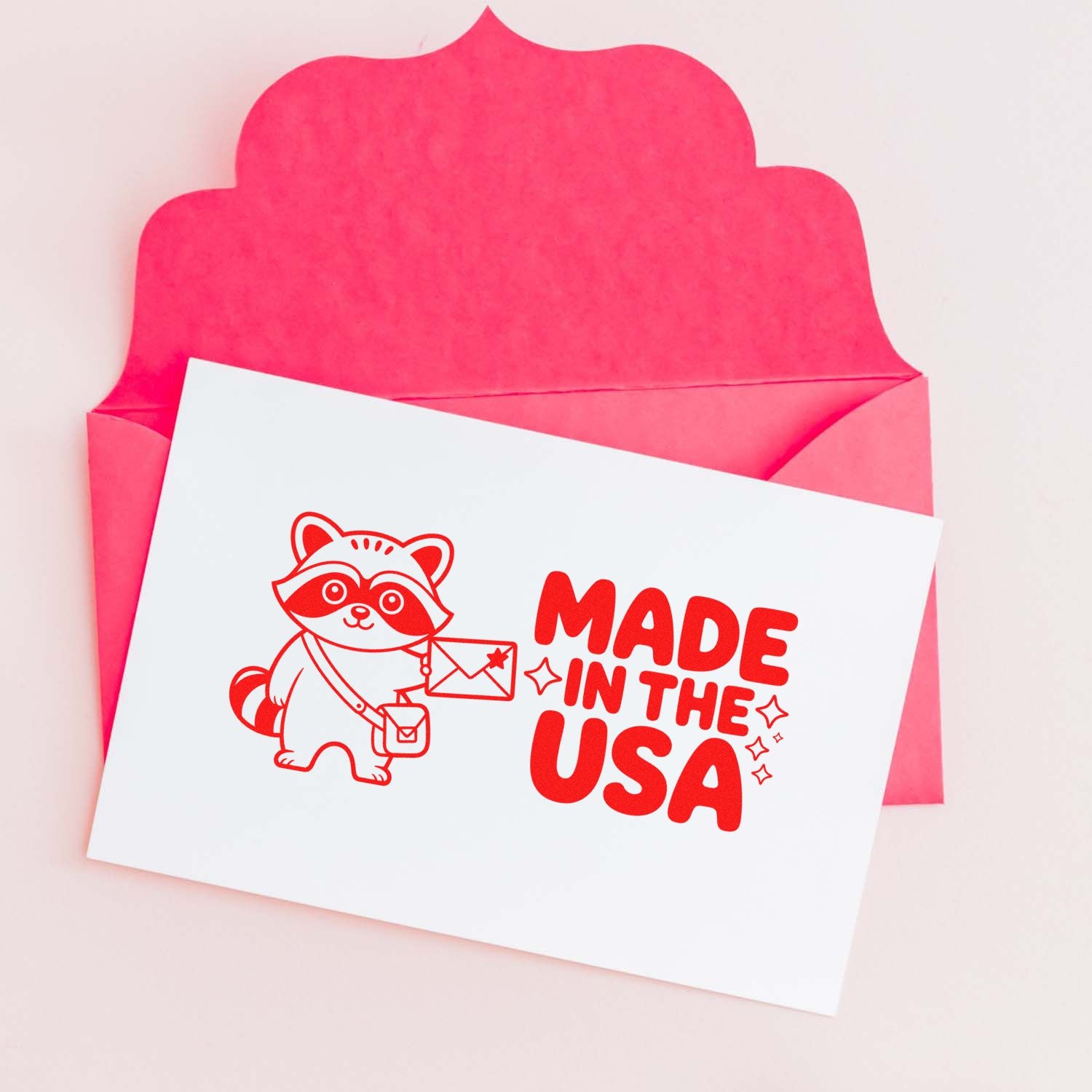 Pink envelope with a white custom stamp and seal card, featuring a red raccoon and Made in the USA text.