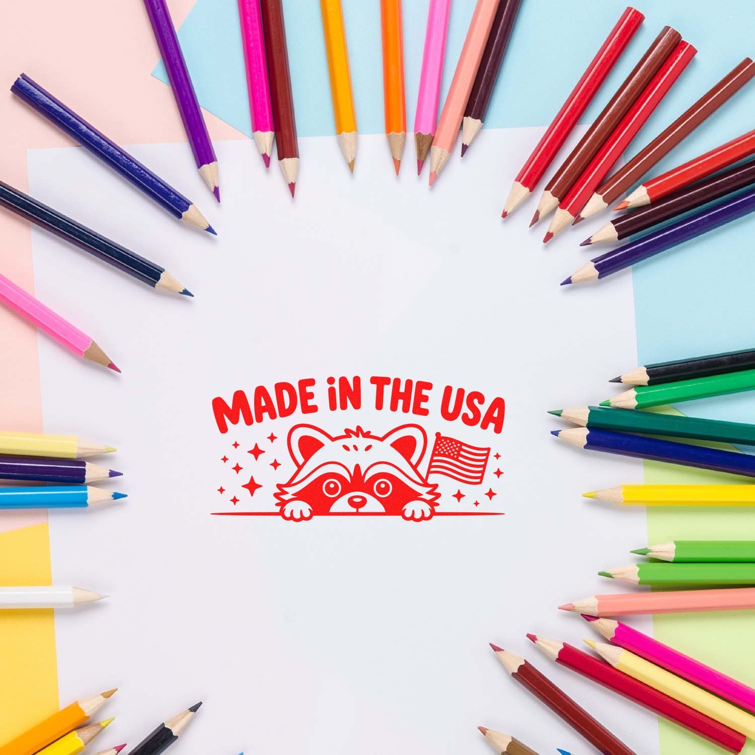 Red Made in the USA raccoon stamp seal surrounded by colorful colored pencils on pastel paper.
