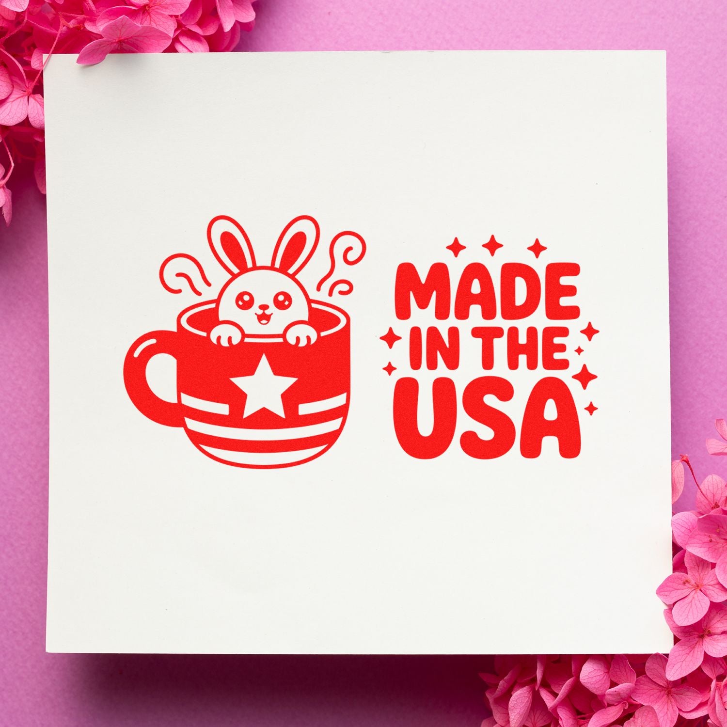 Red Made in the USA stamp and seal design with bunny in a cup, on white paper surrounded by pink flowers.