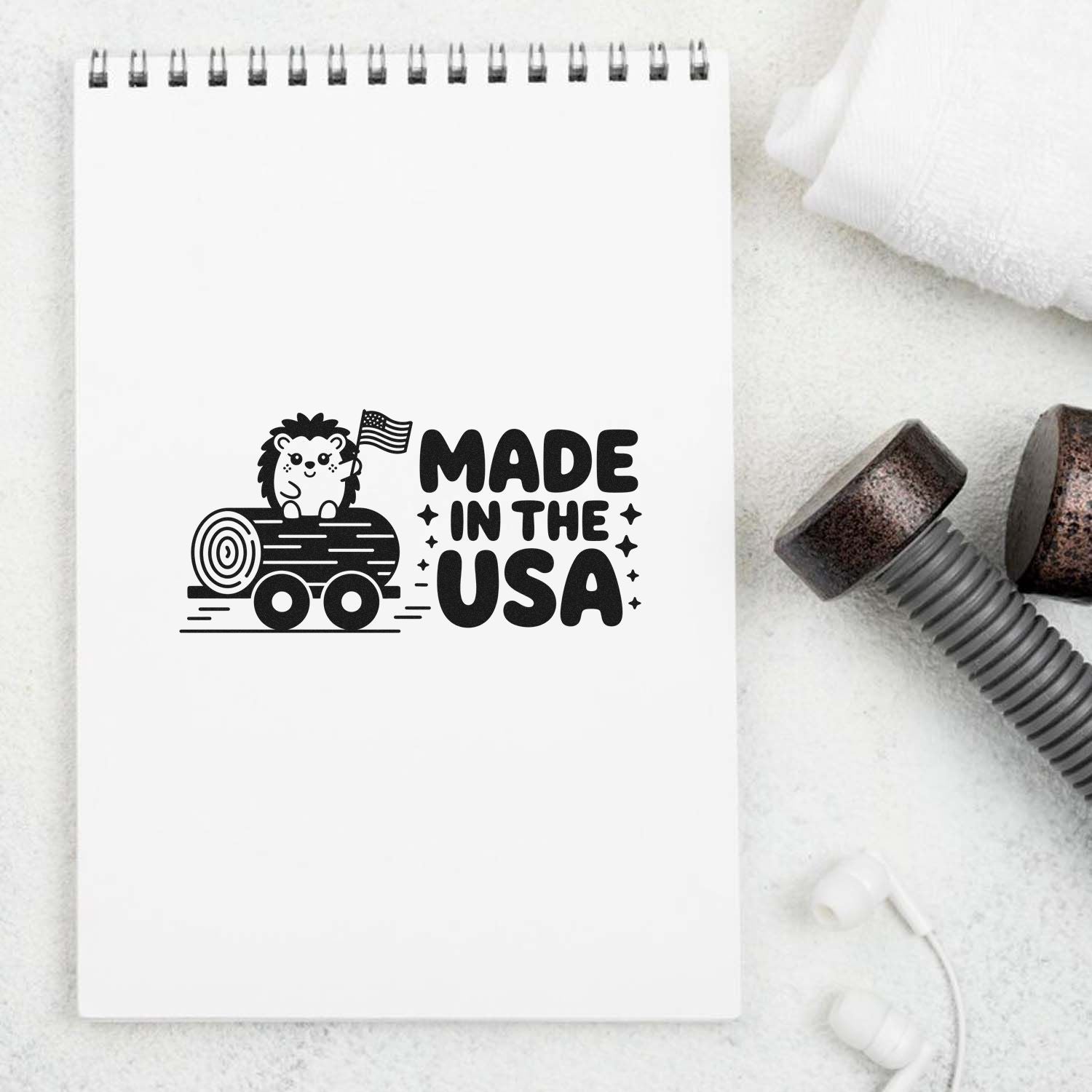 Black Made in the USA stamp design with hedgehog on log and American flag on a white spiral notebook, beside wood stamp seal.