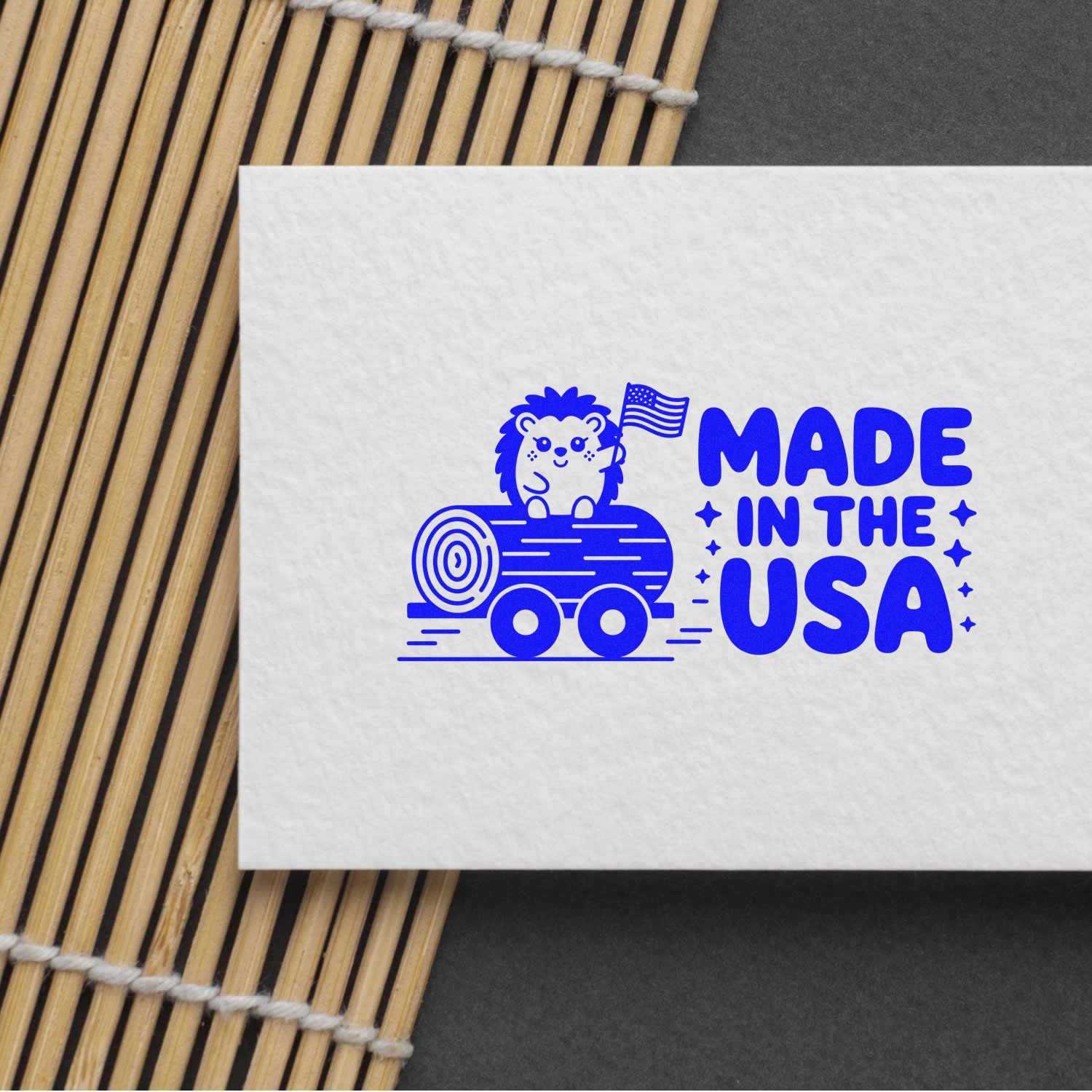 Blue Made in the USA stamp seal with hedgehog on log and American flag, printed in blue on white paper over bamboo mat.