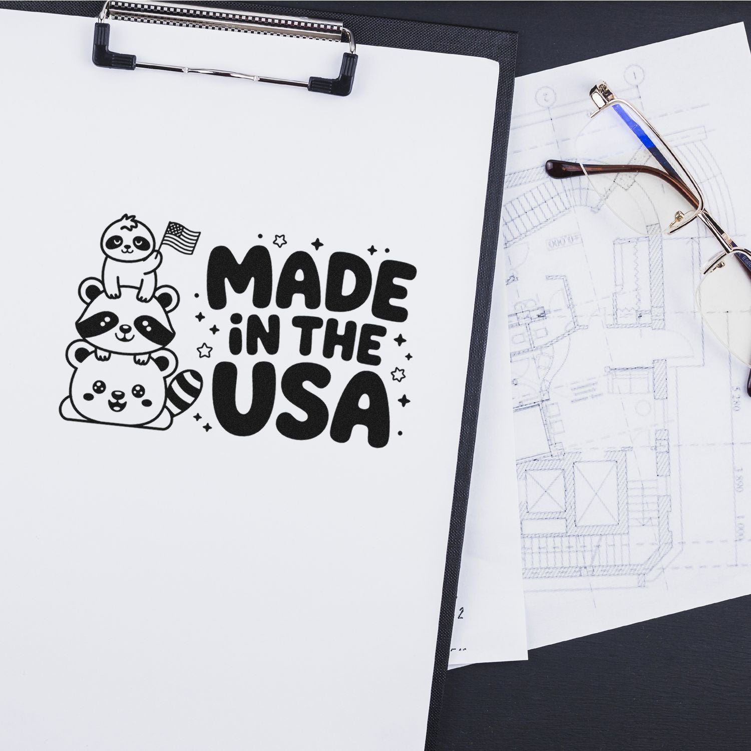 Black stamp and seal design on white paper reading Made in the USA with cartoon raccoons, beside eyeglasses and blueprints.