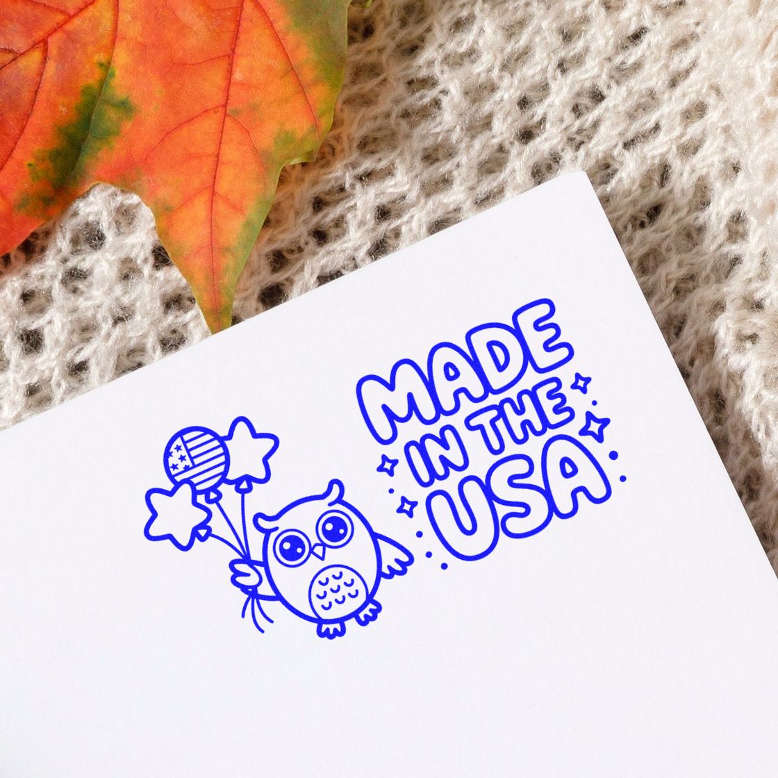 Blue Made in the USA stamp and seal design with owl holding star balloons on white paper, on a cozy knit background.