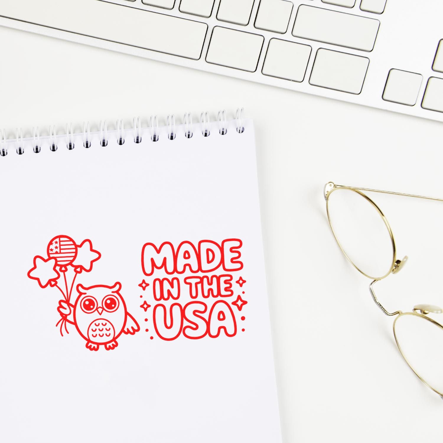 Red Made in the USA stamp seal with owl and balloons on a white notepad beside a keyboard and gold glasses.
