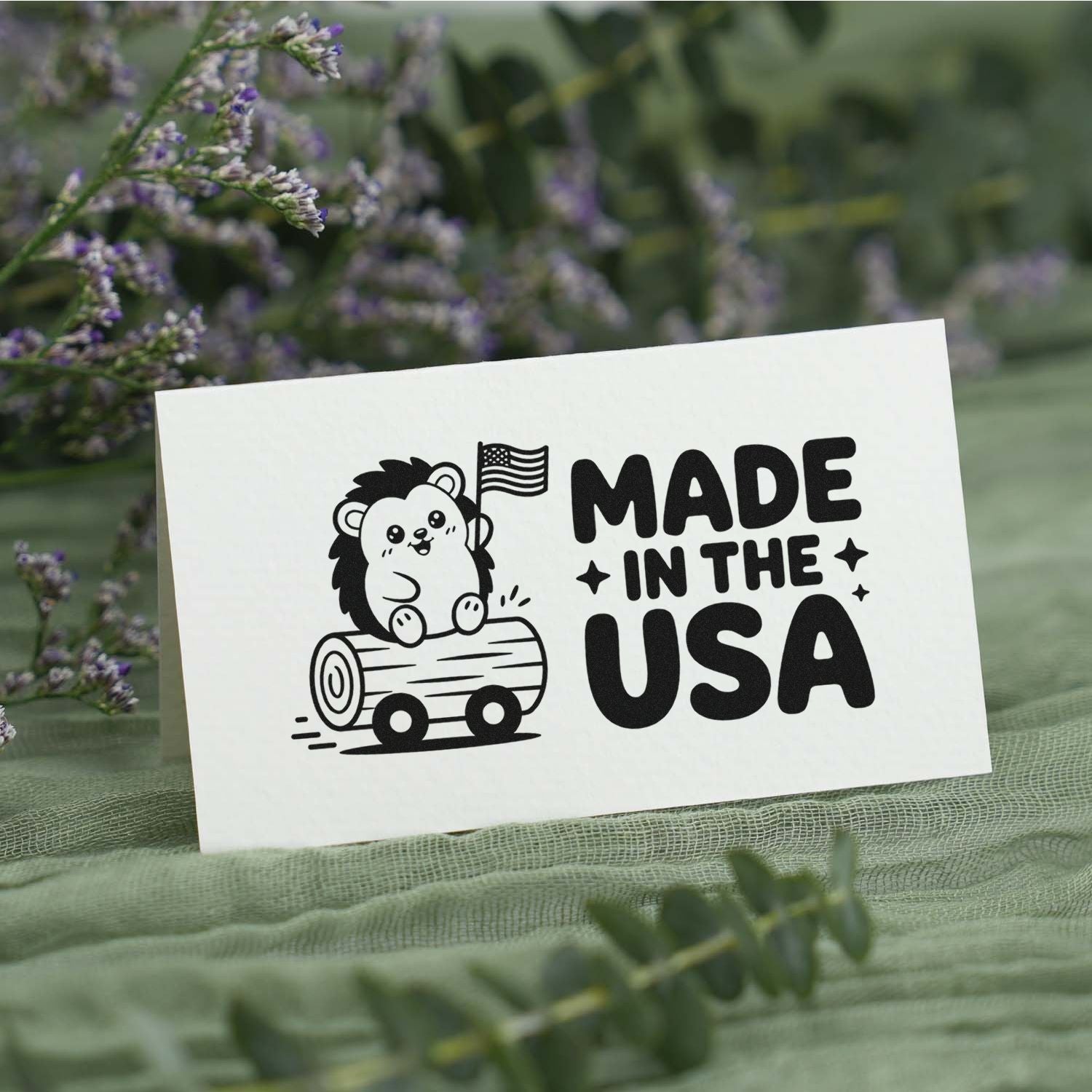 Black custom stamp/seal with cartoon bear on log and Made in the USA text, on white paper with green floral background.
