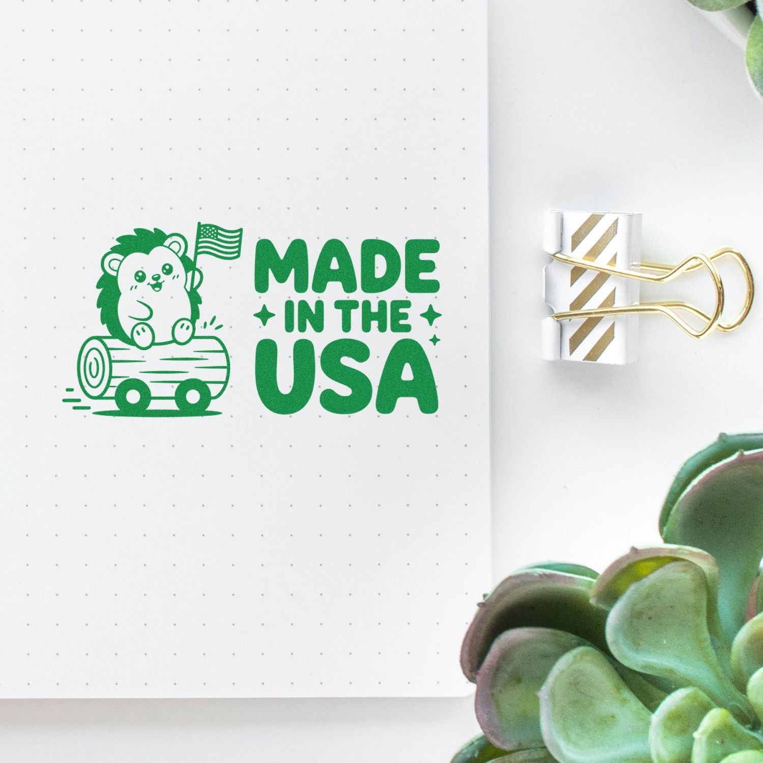 Green Made in the USA rubber stamp with bear on log, on white dotted paper beside a gold binder clip.