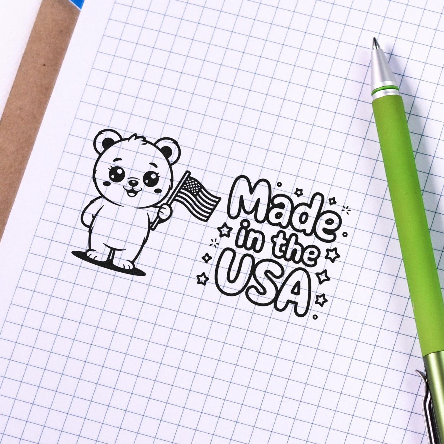 Black bear stamp and seal with U.S. flag and Made in the USA on graph paper, beside a green pen.
