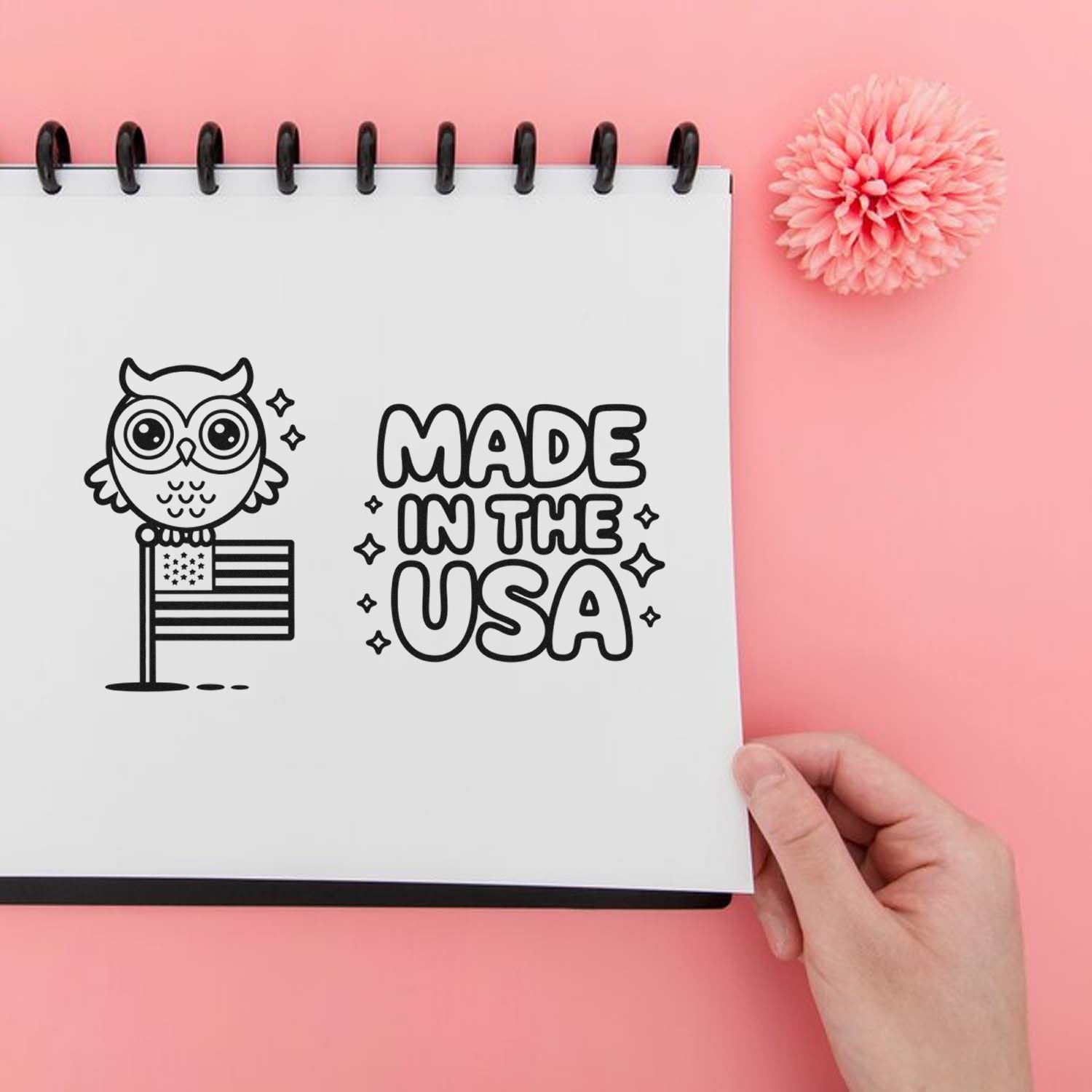Custom black stamp and seal design reading Made in the USA with owl and flag on a white notebook, on a pink background.