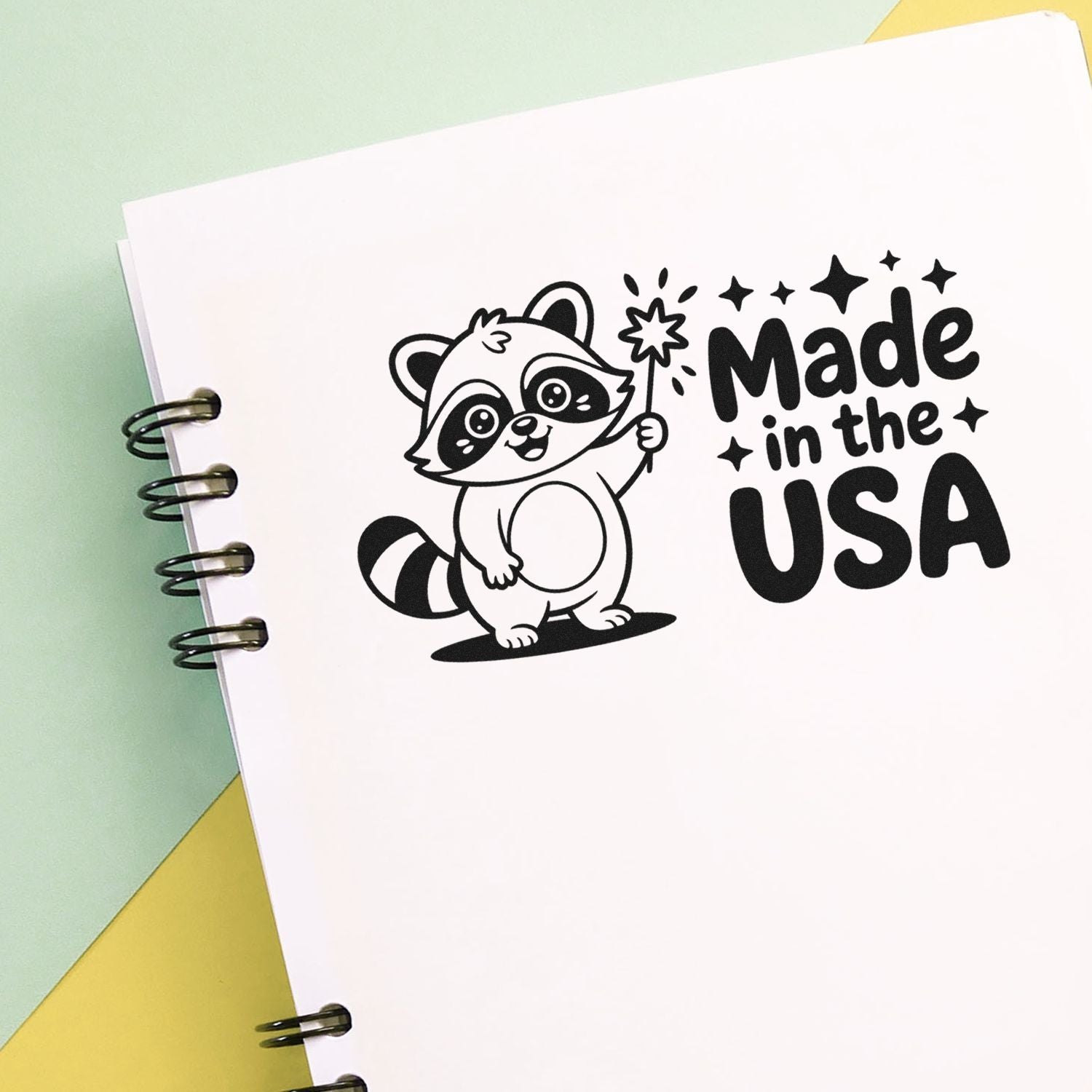 Black raccoon stamp and seal design reading Made in the USA on white paper with mint green and yellow background.