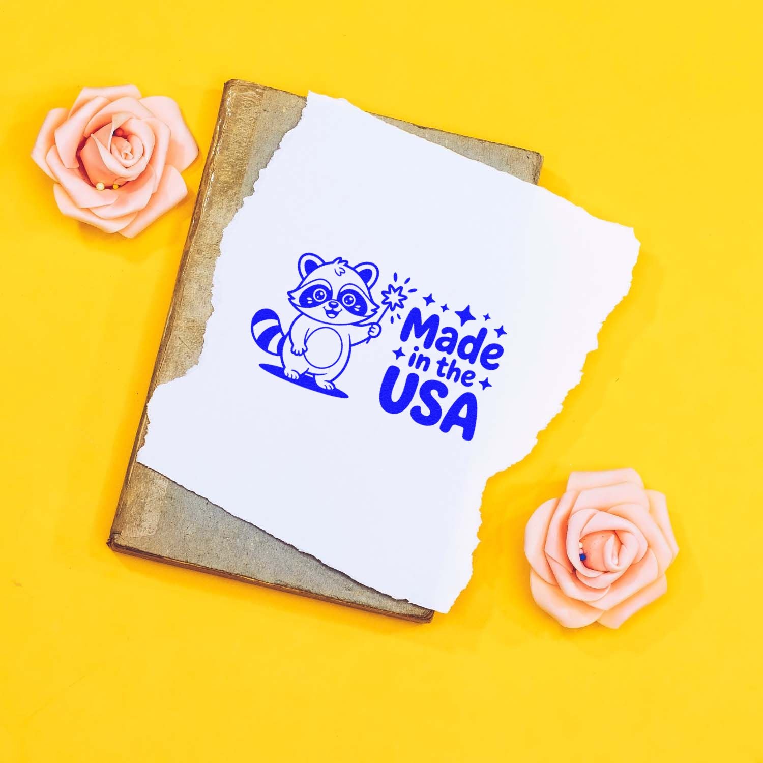 Blue Made in the USA stamp seal on torn white paper over a vintage book, with pink roses on a bright yellow background.