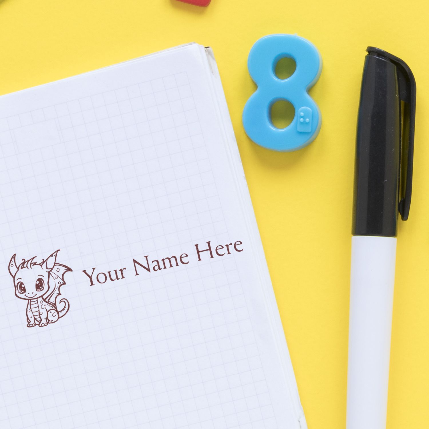 Blue number 8 name stamp, black-and-white pen, and custom dragon seal on grid notebook against a yellow background.