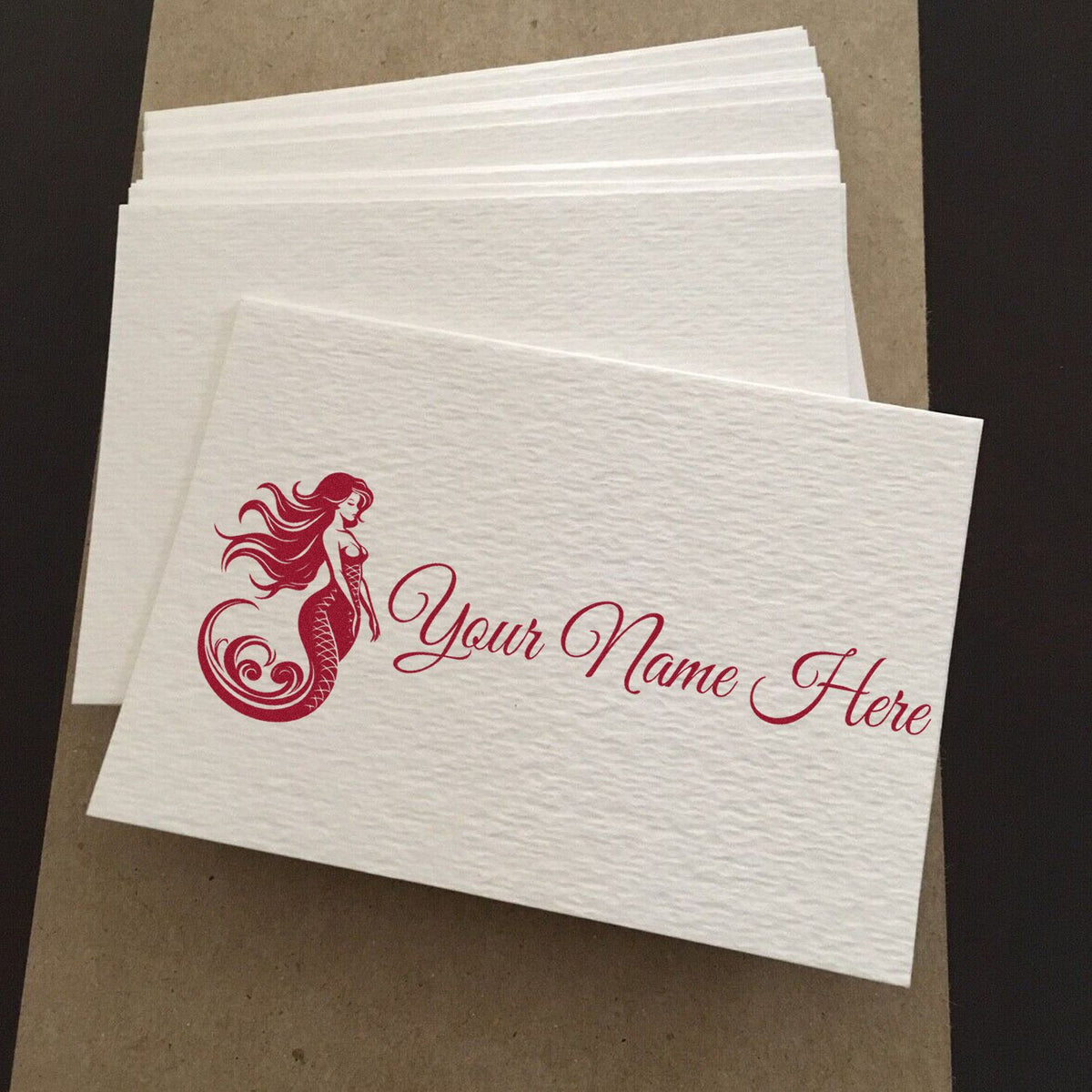 White textured custom stamp and seal sheets with burgundy mermaid logo and Your Name Here script on layered paper.