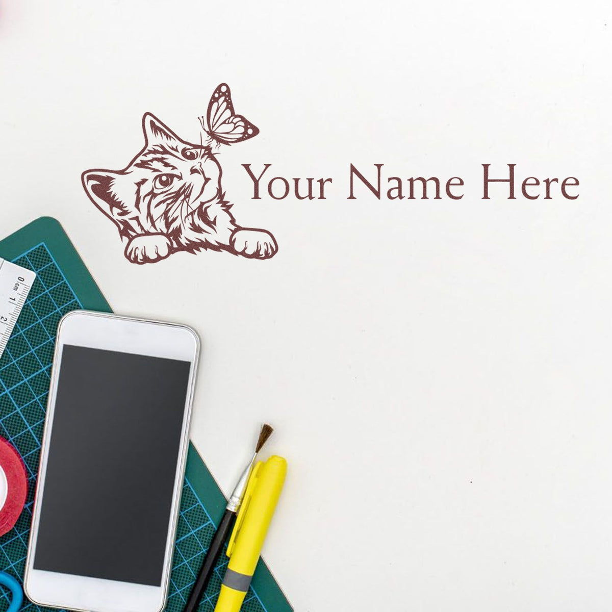 Custom brown cat-and-butterfly stamp seal with Your Name Here text on white background, beside craft tools.