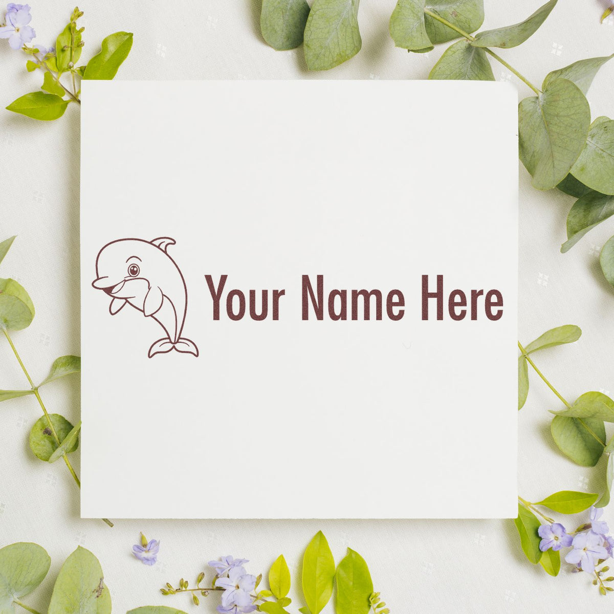 Custom stamp and seal mockup with brown dolphin logo and "Your Name Here" on white card, framed by green leaves and lavender flowers.