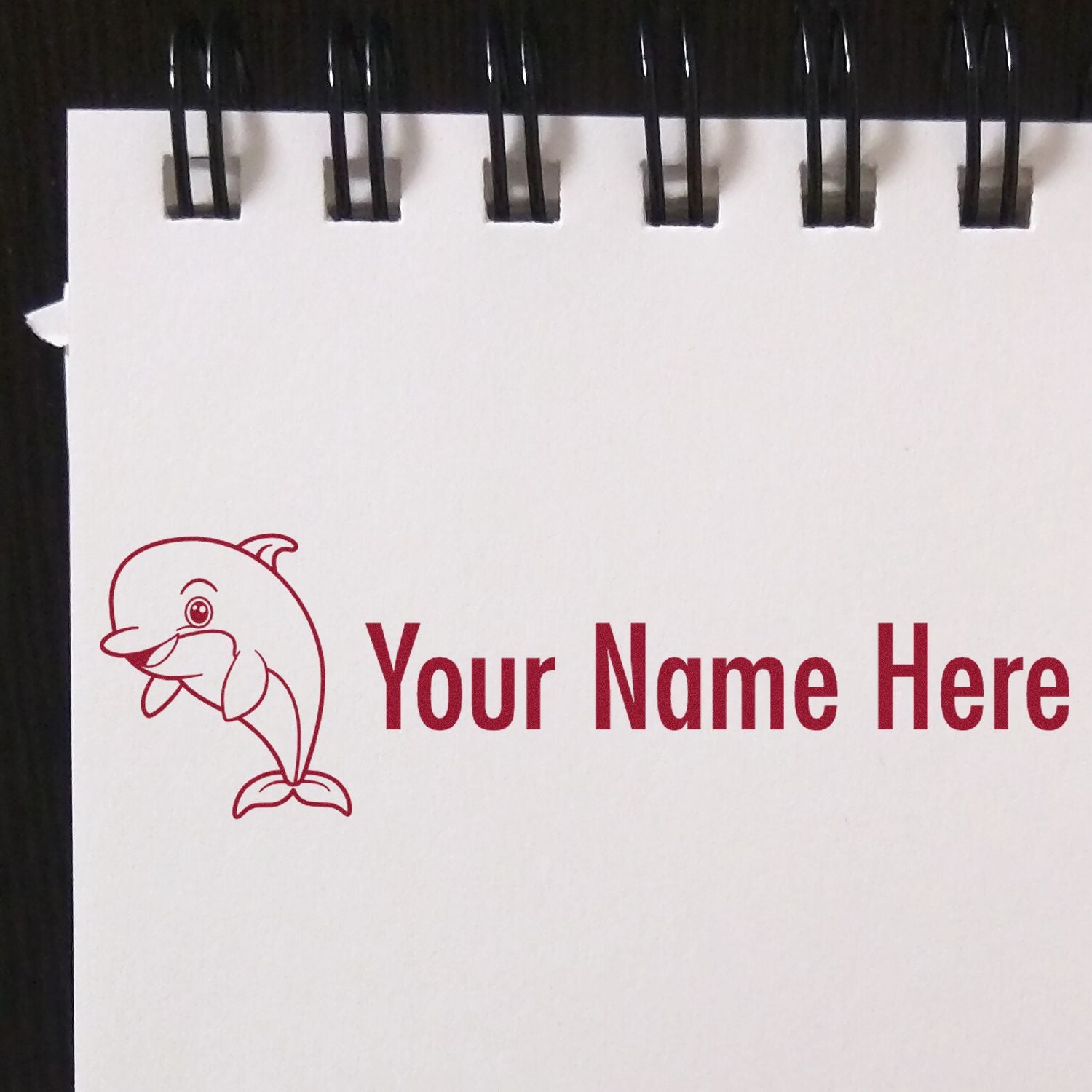 Red custom stamp and seal design with dolphin logo and Your Name Here on a white spiral-bound page.