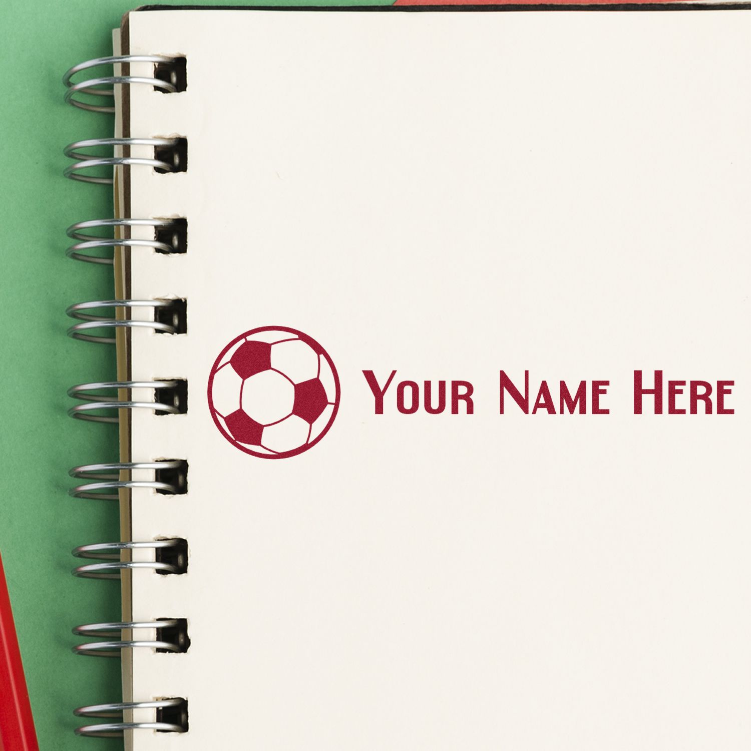 Cream spiral notebook page with burgundy soccer-ball stamp seal and custom text Your Name Here on green background.