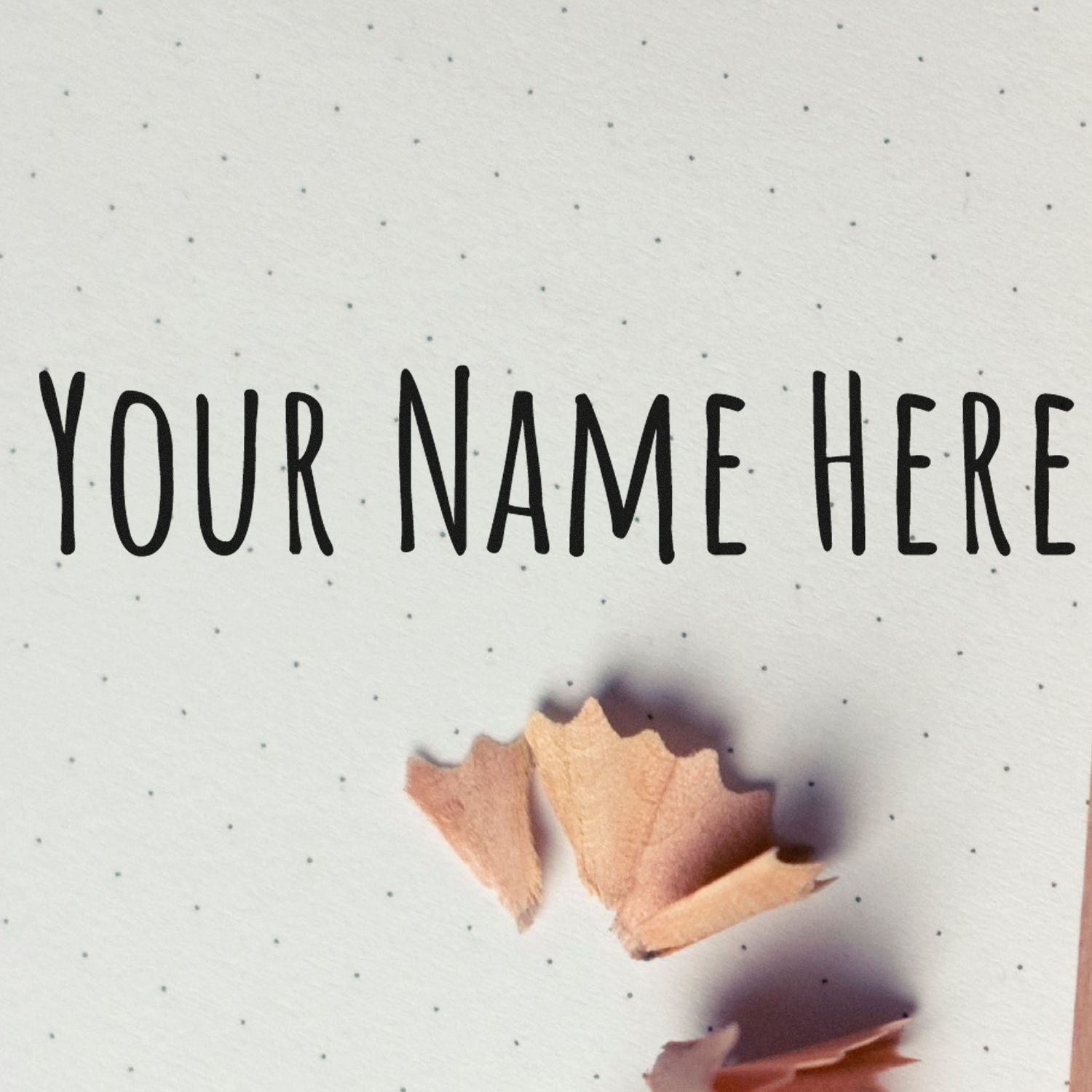 Custom stamp and seal sample with black YOUR NAME HERE text on white dotted paper and light wood shavings.