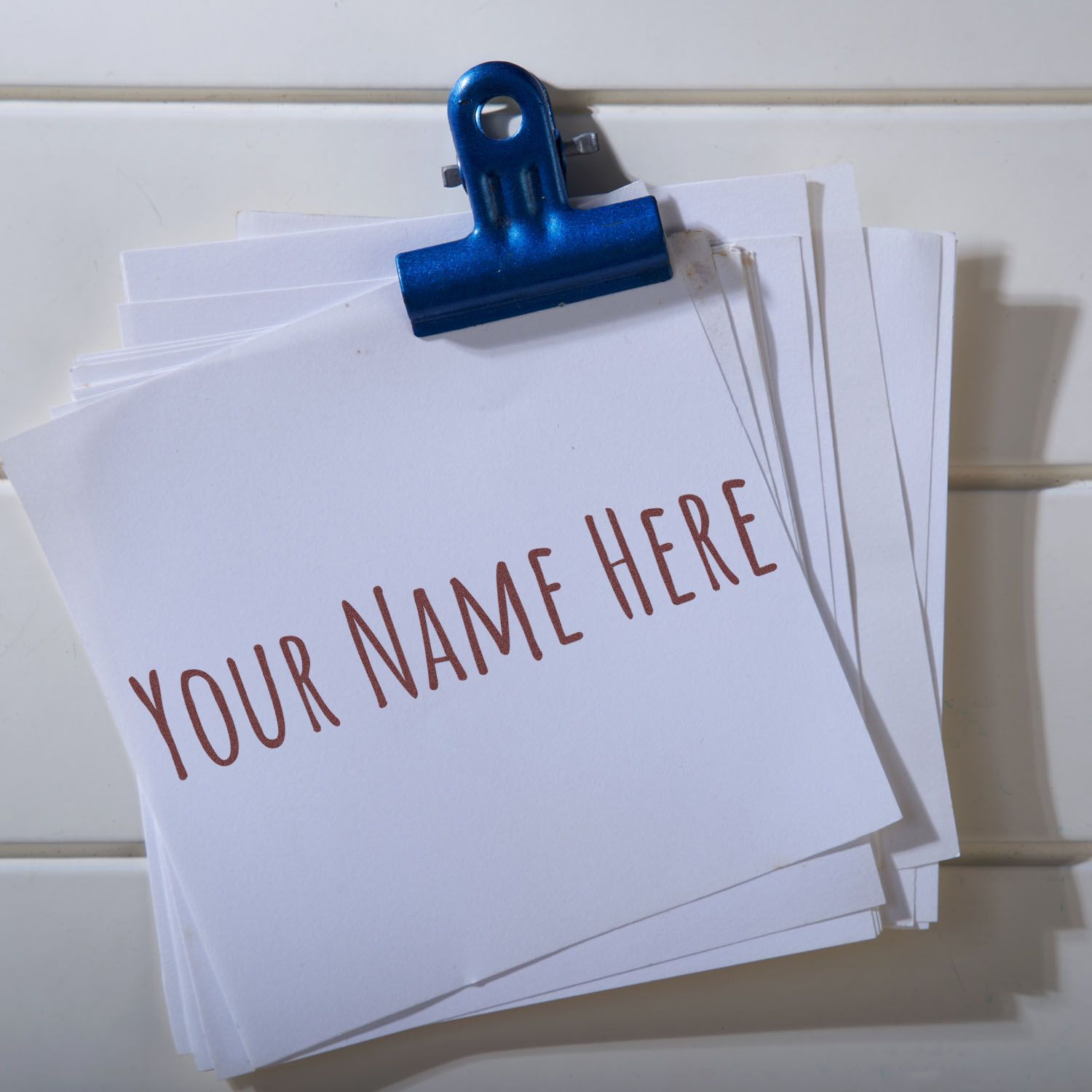 Blue binder clip holding white custom stamp and seal cards with brown YOUR NAME HERE text