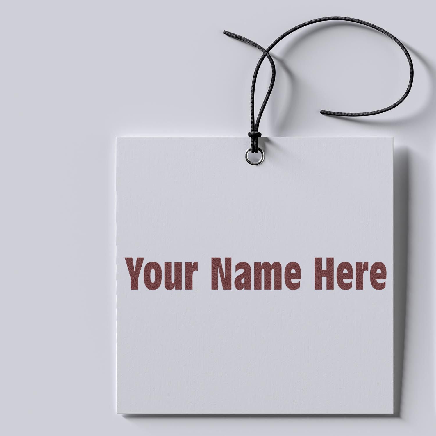 White custom stamp and seal tag with black hanging cord, metal eyelet, and red Your Name Here text on light gray.
