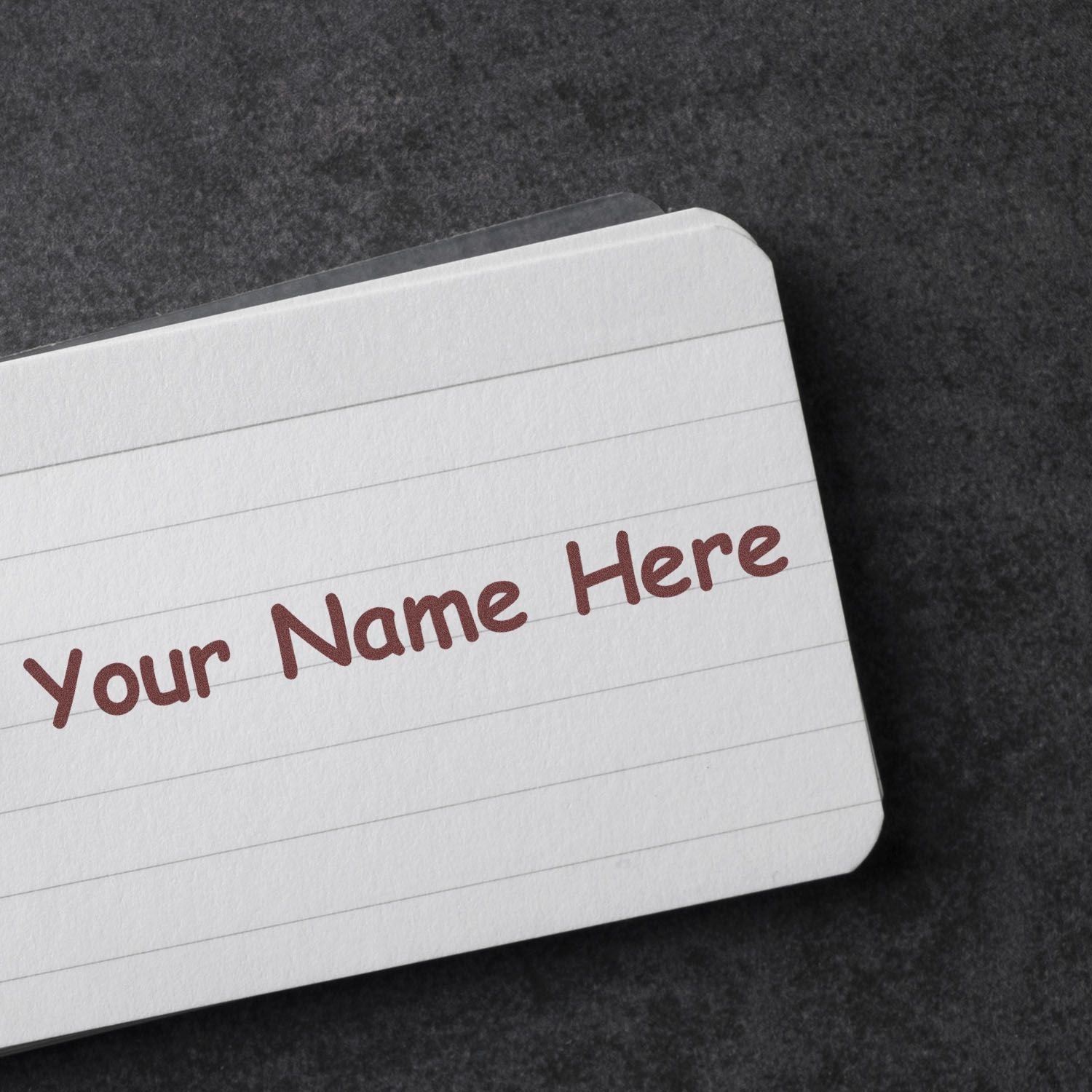Custom stamp and seal text 'Your Name Here' in maroon on a white lined card against a dark textured background.