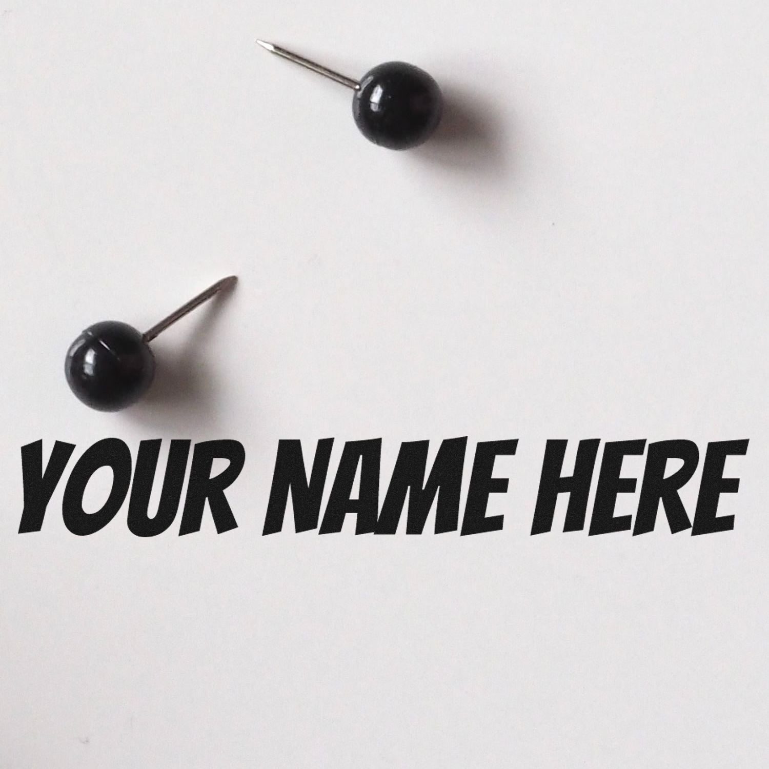 Black round stamp and seal products with metal pins on white background and bold YOUR NAME HERE text