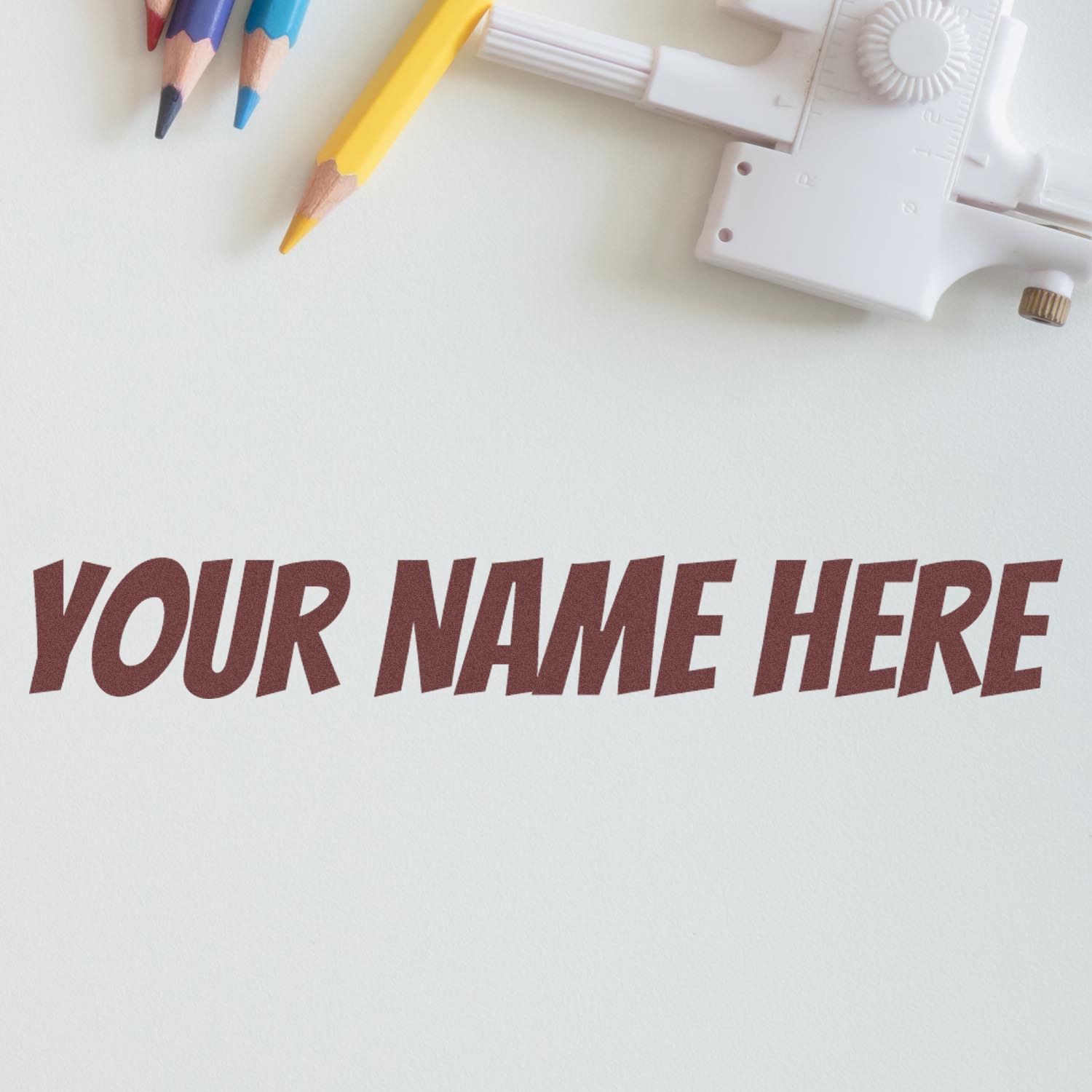 White custom stamp and seal embosser with brown YOUR NAME HERE imprint and colored pencils on a white background.