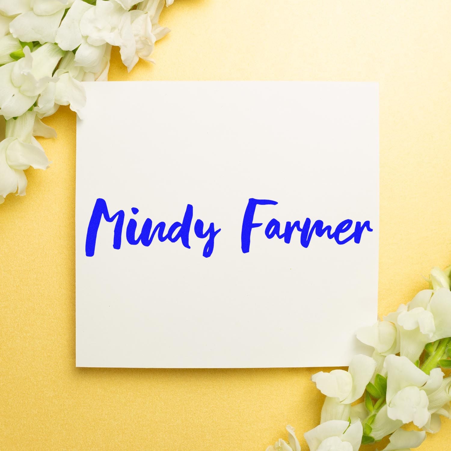 Blue custom stamp and seal with handwritten Mindy Farmer on white card, framed by white flowers on a yellow background.