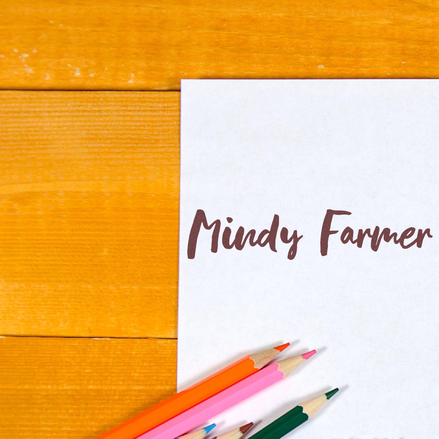 Custom stamp and seal products for Mindy Farmer on a white card, with brown script and colored pencils on orange wood.