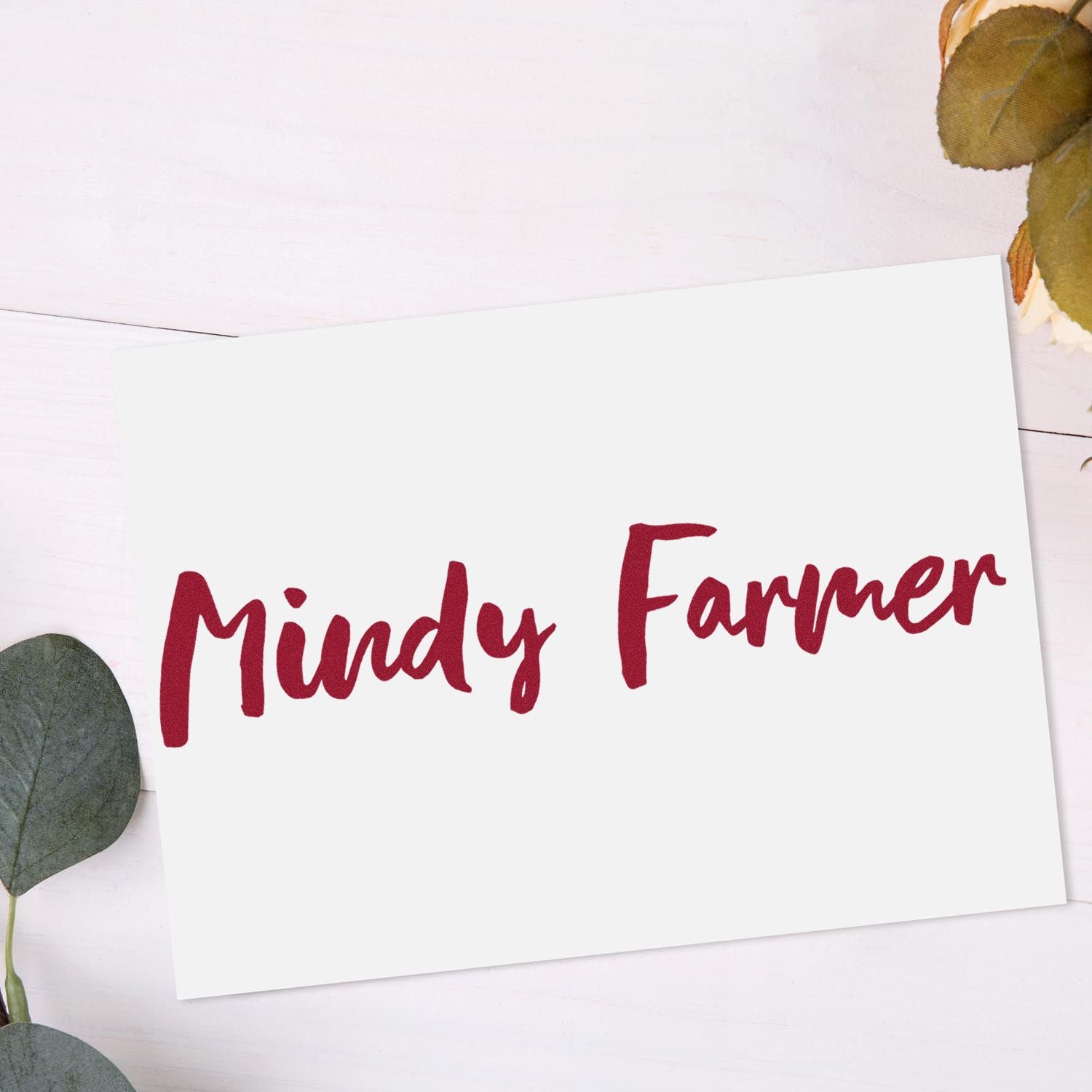 White card with burgundy Mindy Farmer custom stamp and seal, styled on light wood with eucalyptus leaves.