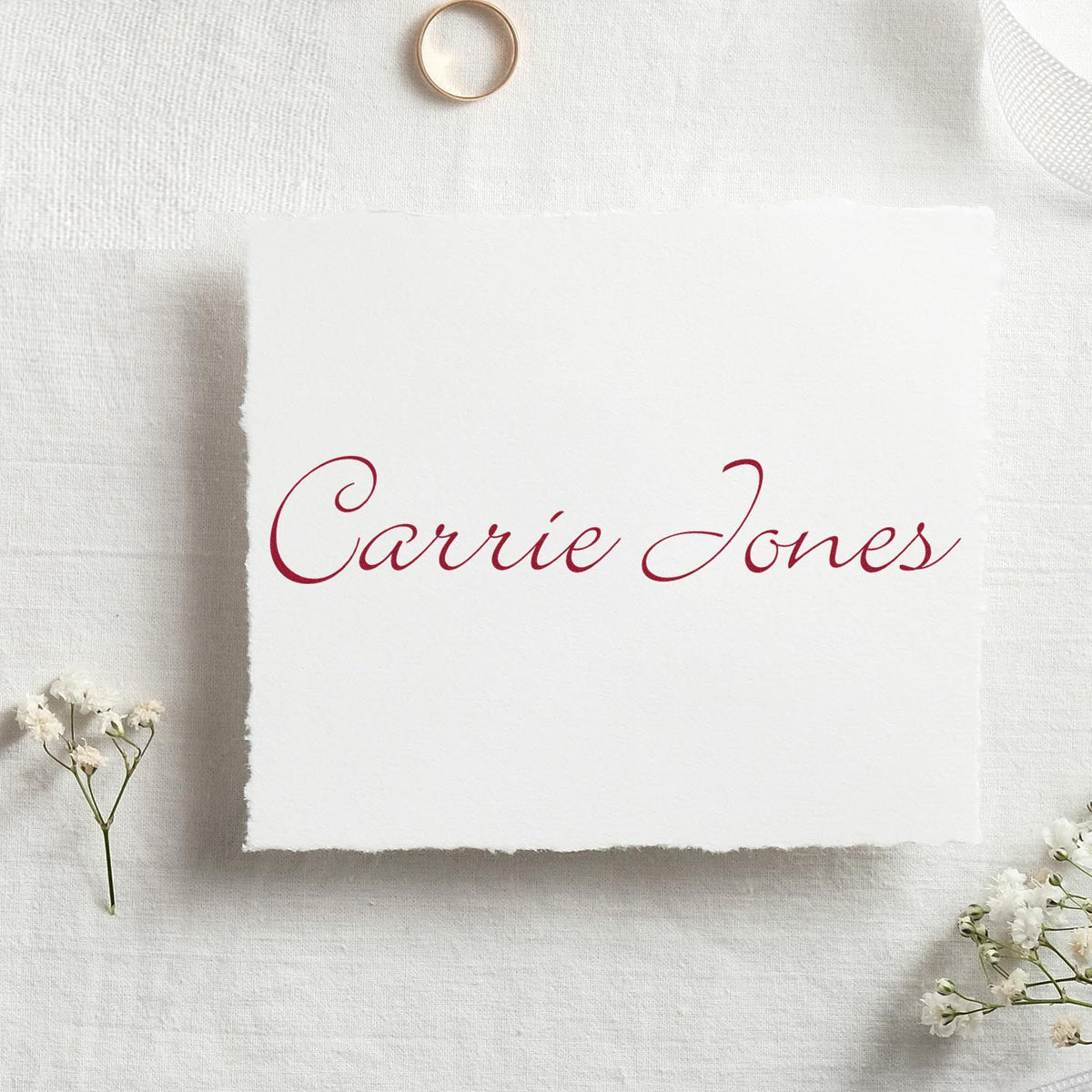 Burgundy calligraphy custom stamp and seal on white deckled paper, styled on cream linen with white flowers.