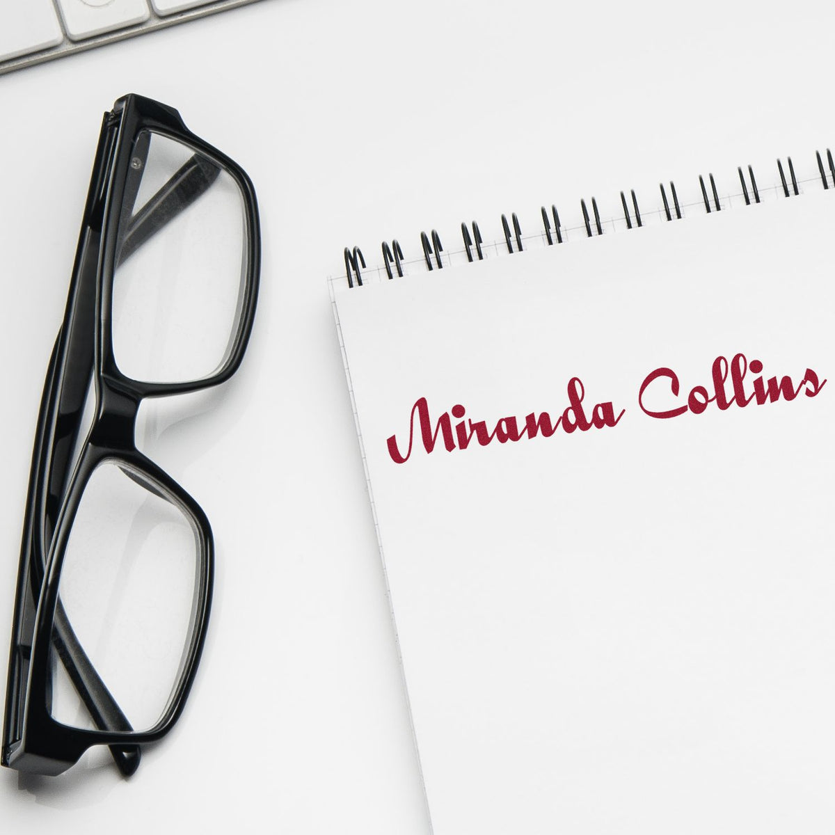 Black eyeglasses beside a white spiral notebook with red Miranda Collins custom stamp and seal branding.
