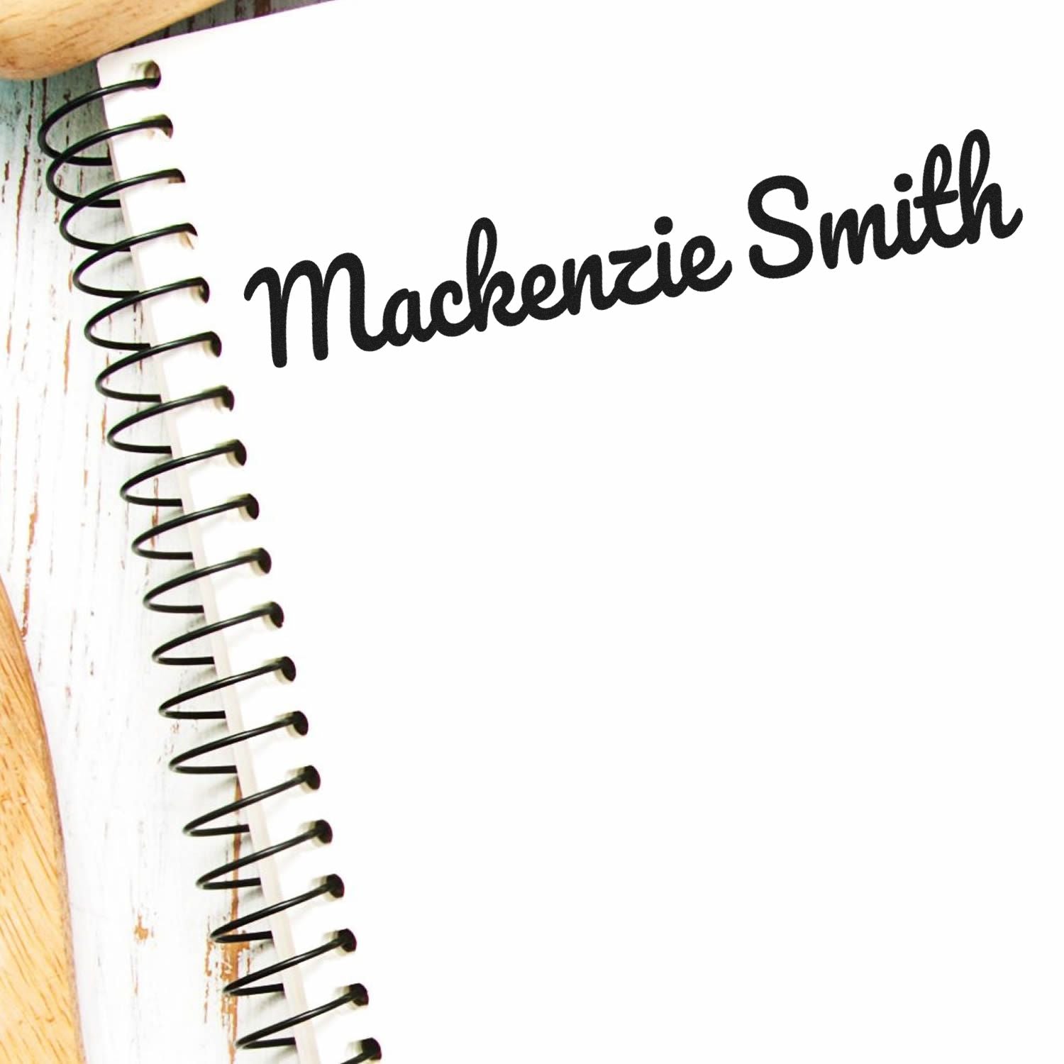 Black custom name stamp and seal reading Mackenzie Smith on a white spiral notebook page