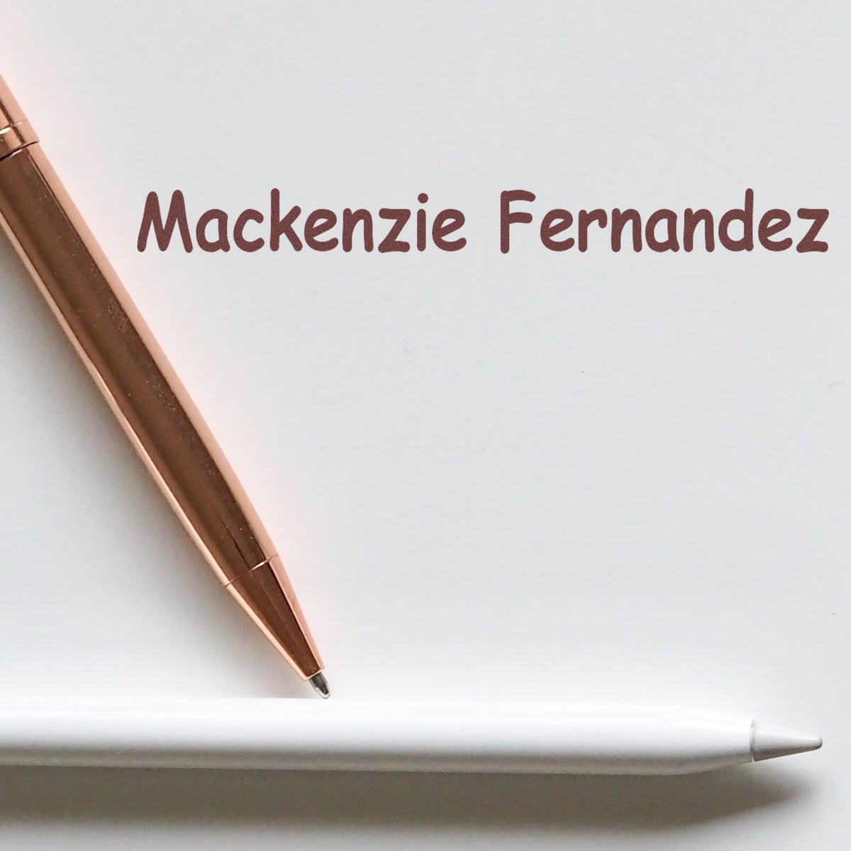 Rose gold custom stamp and seal set with maroon Mackenzie Fernandez text and white pen on a white background.