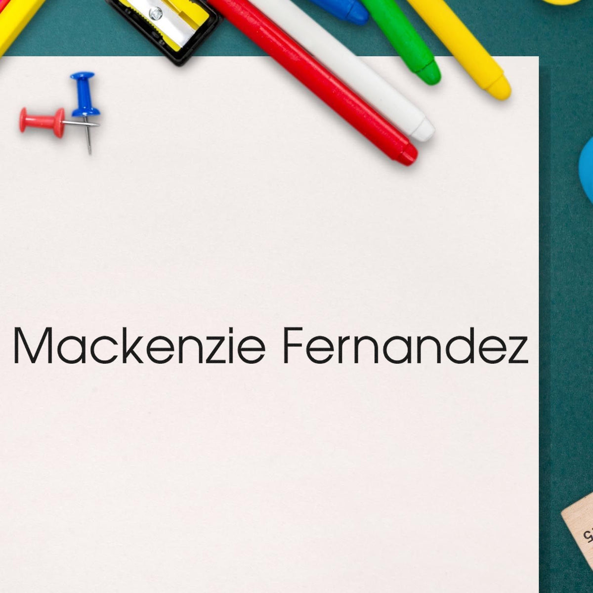 Custom stamp and seal for Mackenzie Fernandez on white paper, with colorful red, blue, green, and yellow pens and push pins.