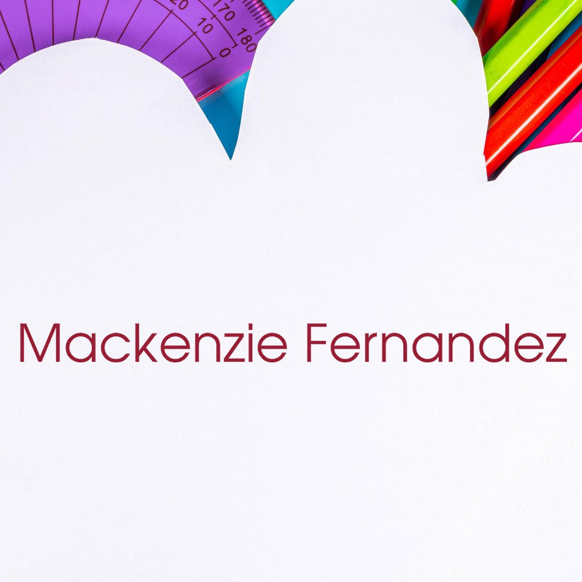 Custom stamp and seal with Mackenzie Fernandez in red on white, surrounded by colorful pens and a purple protractor.