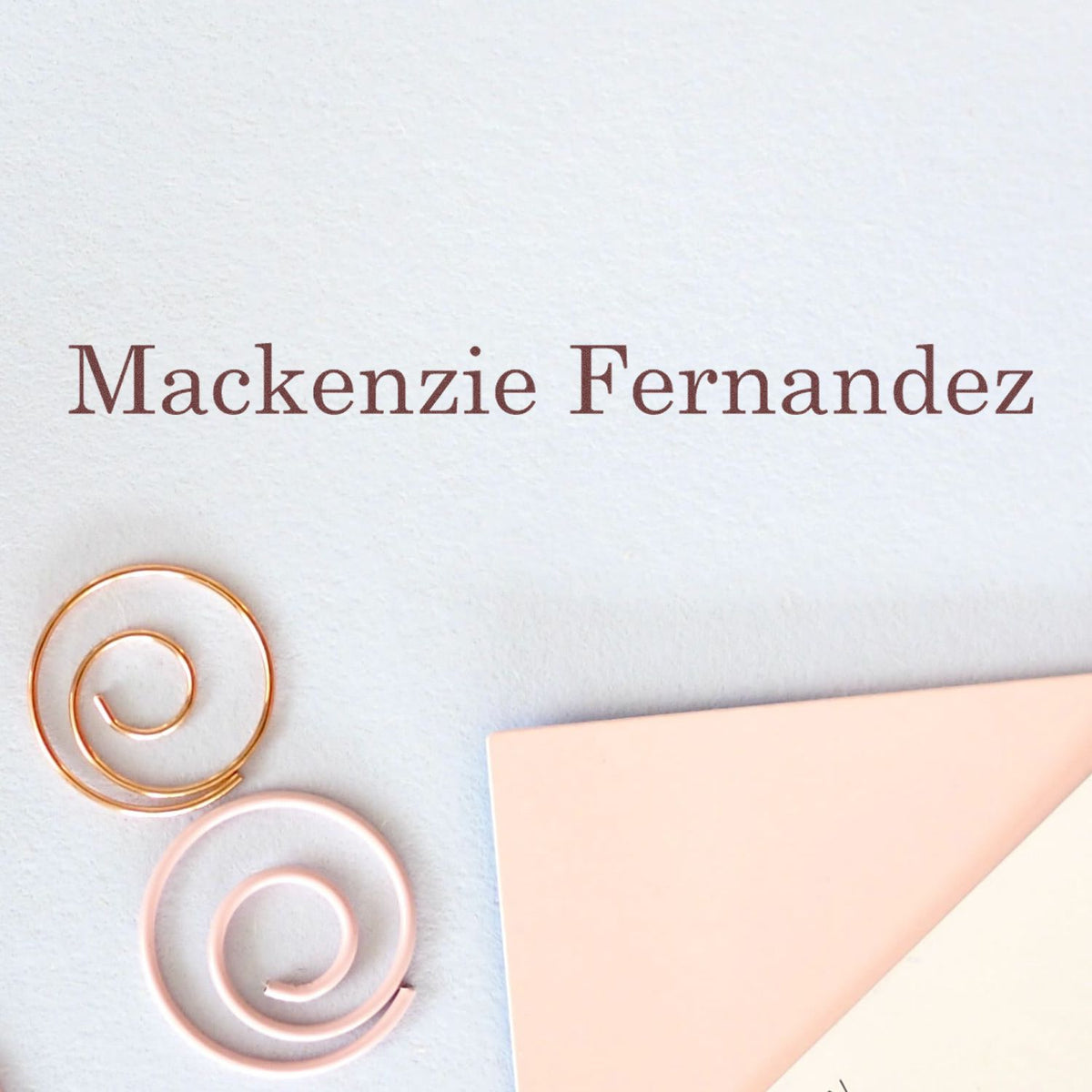 Maroon Mackenzie Fernandez text with gold and rose-gold spiral stamp seals on white paper and a blush pink envelope corner.