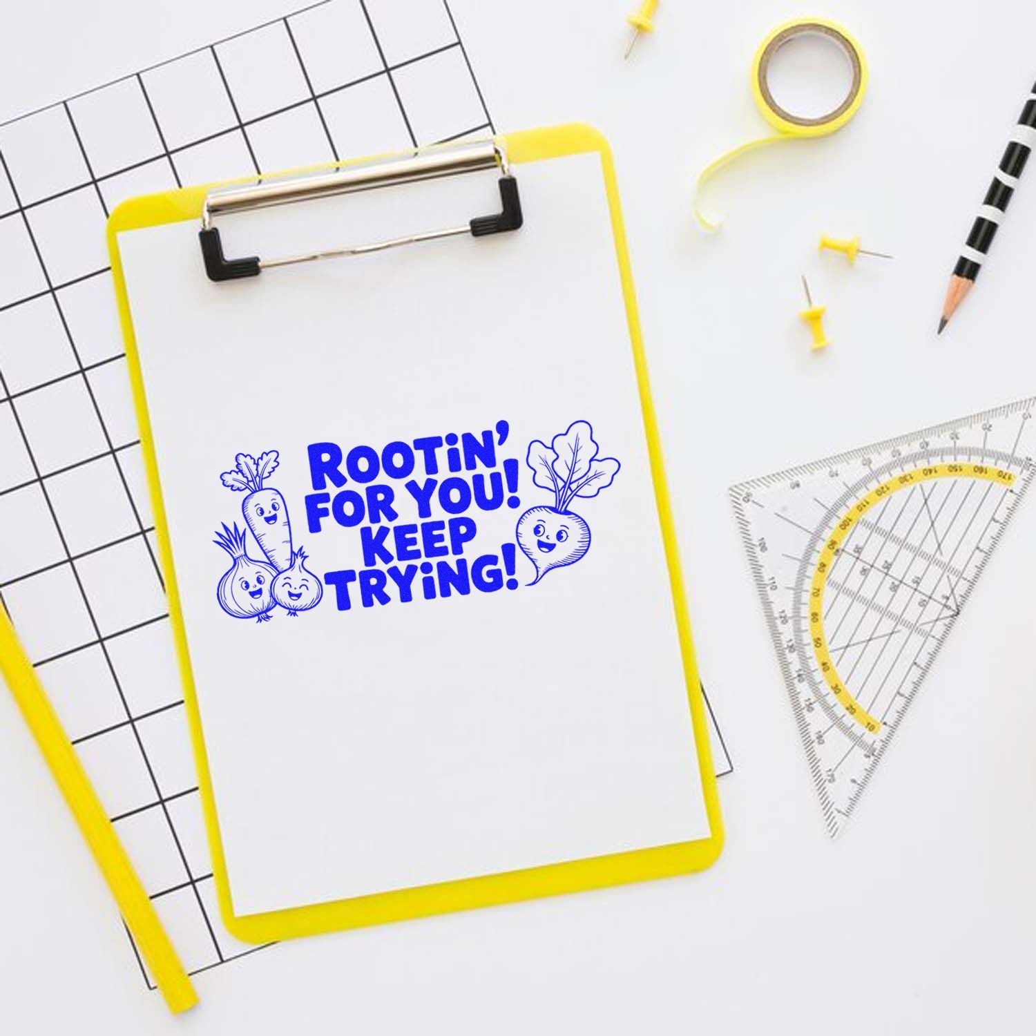 Yellow clipboard with blue rubber stamp/seal design reading Rootin for you! Keep trying! with smiling veggie doodles.