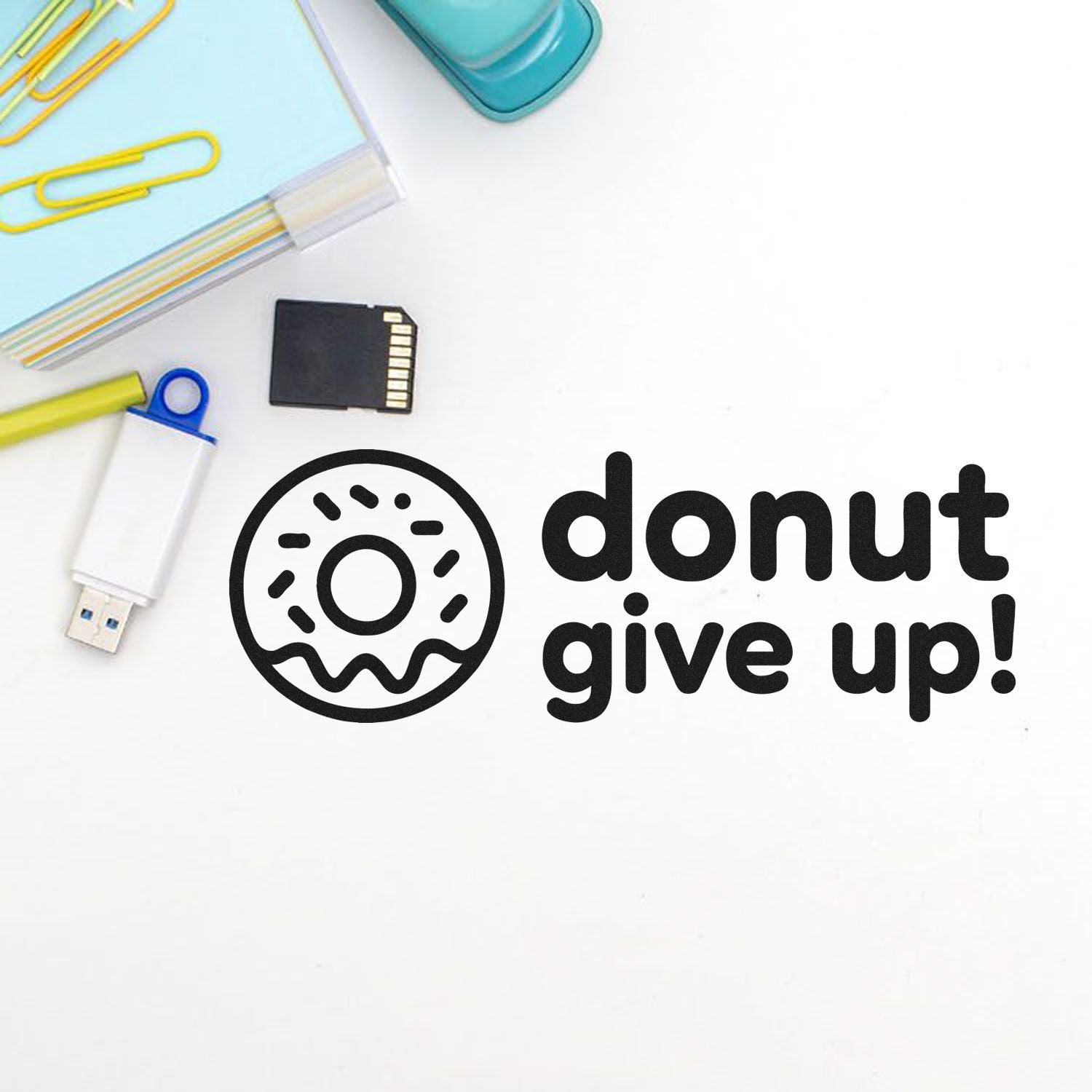 Black donut seal stamp reading donut give up! with pastel blue, yellow, and white office accessories and memory cards.