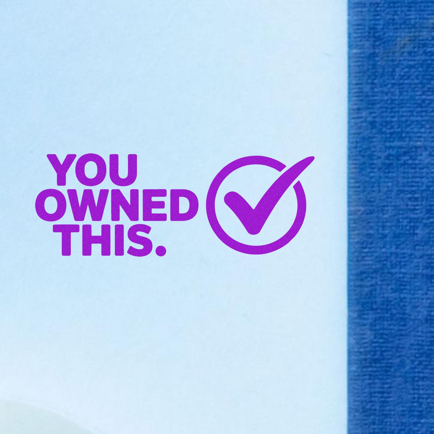 Purple stamp and seal reading YOU OWNED THIS. with checkmark on white paper beside blue fabric.