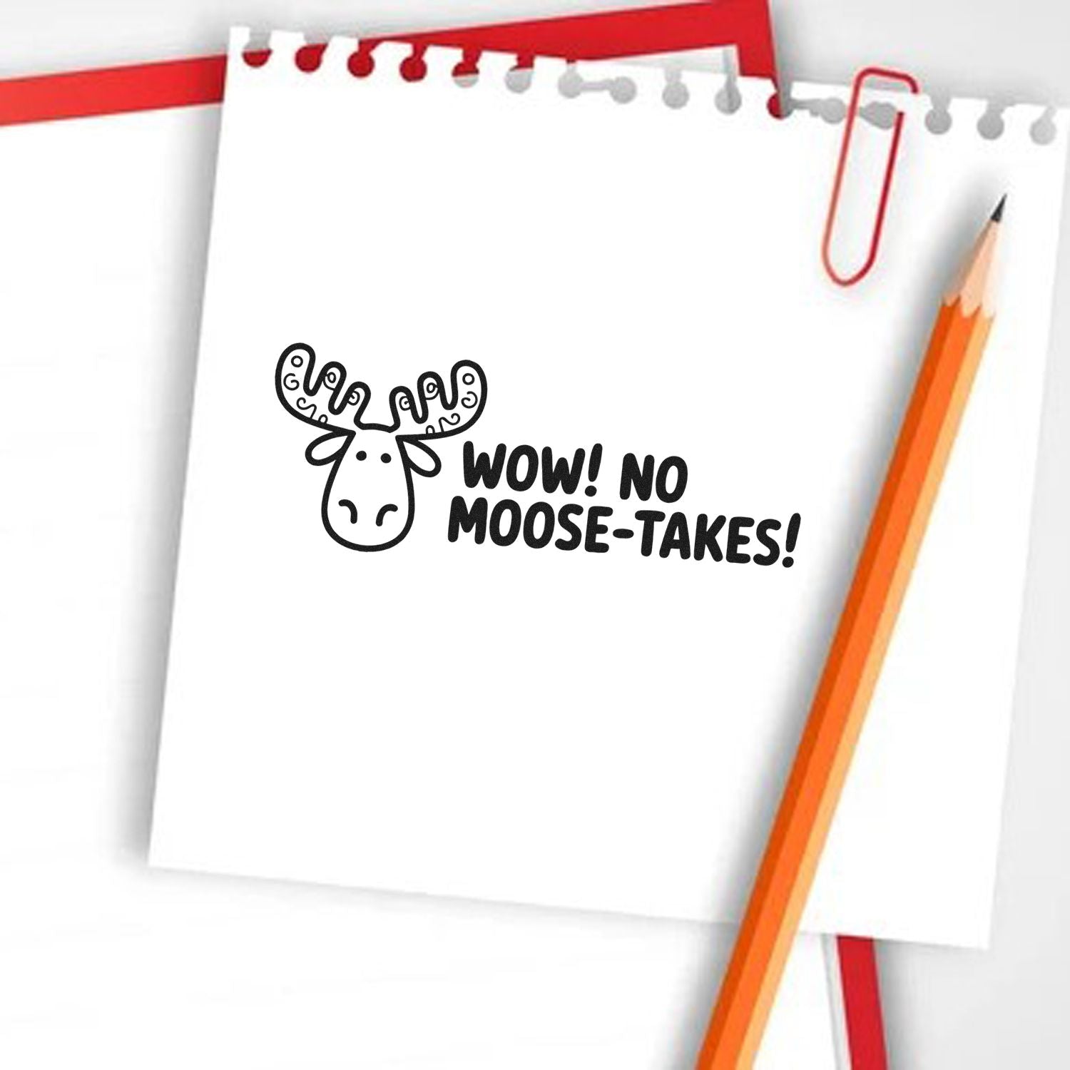 Black moose rubber stamp with WOW! NO MOOSE-TAKES! on white notepad, with orange pencil and red paperclip.